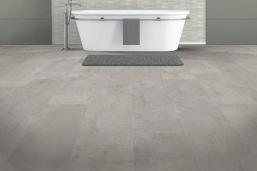 Modern bathroom with a freestanding white tub, gray rug, and large gray tile floor.