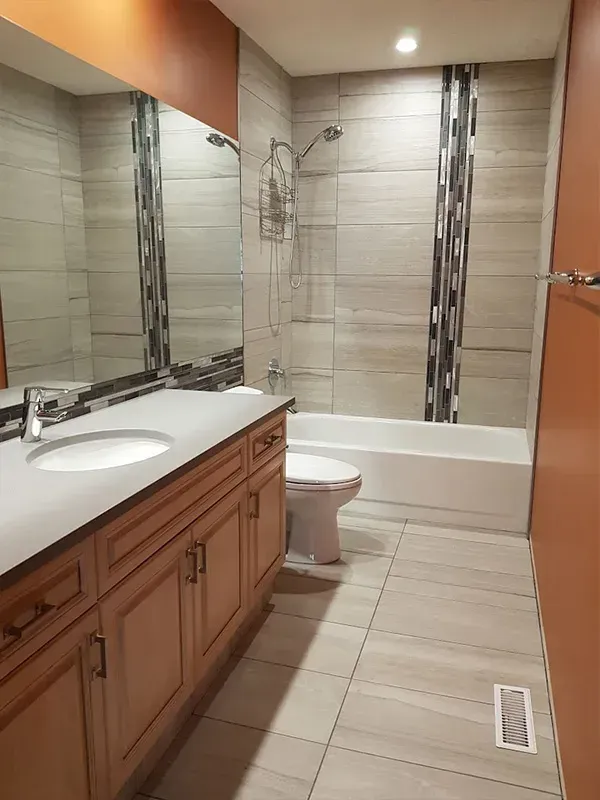 Modern bathroom with wood vanity, large mirror, toilet, and tiled tub-shower combo.
