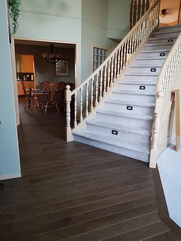 Indoor staircase with white railings and dark wood floors, leading to a dining area.