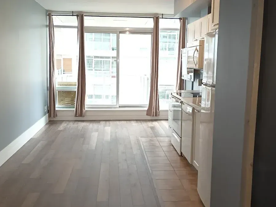 Empty modern apartment living room with large windows and a small kitchen on the right