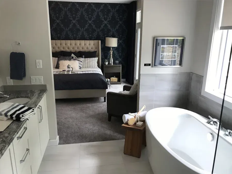 Bedroom and bathroom interior with a bed, dark accent wall, window seat, and freestanding bathtub.