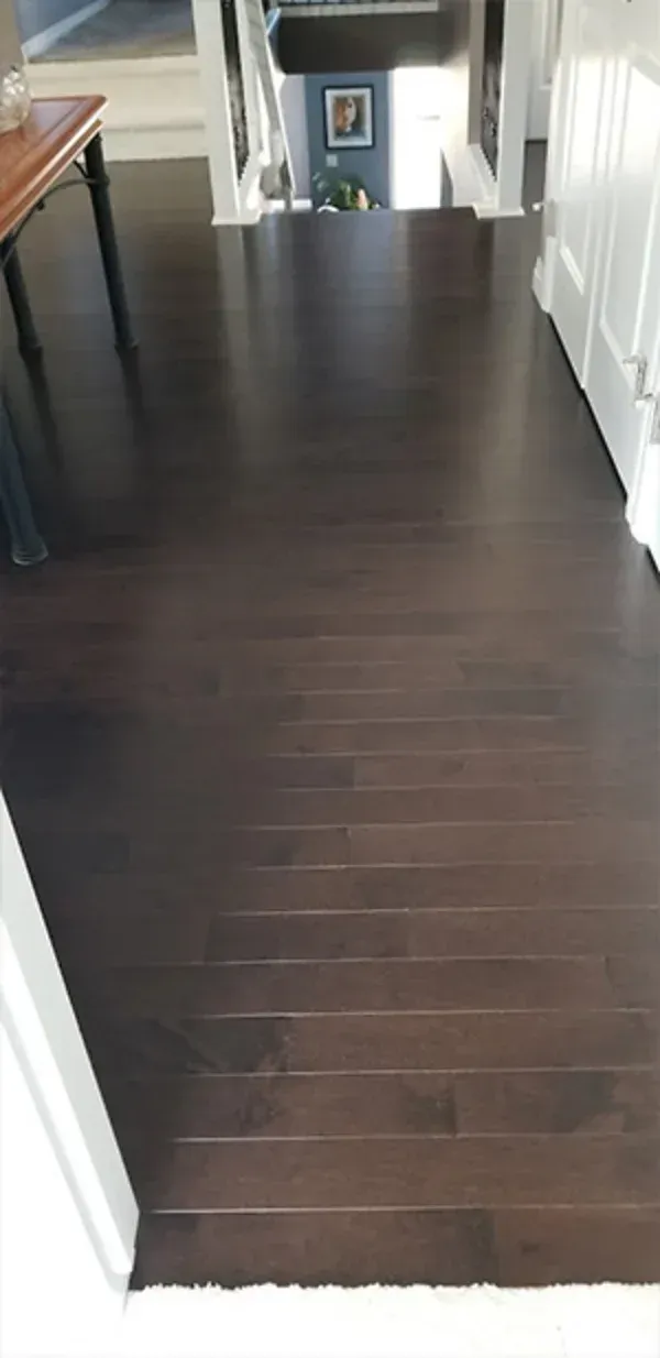 Dark hardwood hallway floor leading to a doorway, with white walls and a railing on the right.