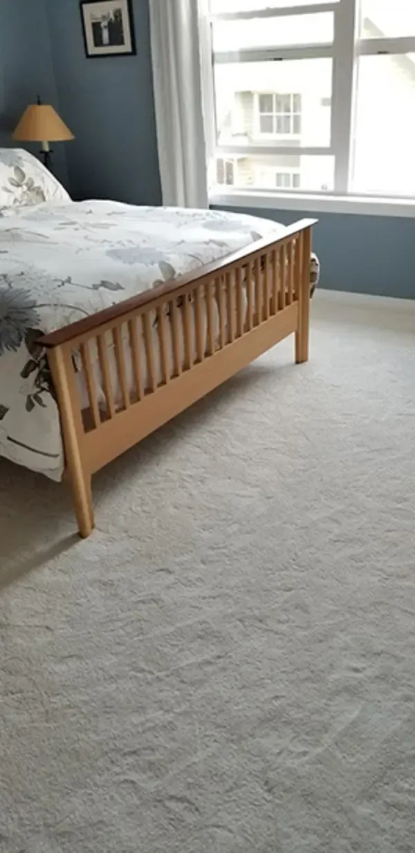 Bedroom with wooden bed, light carpet, and large window letting in daylight