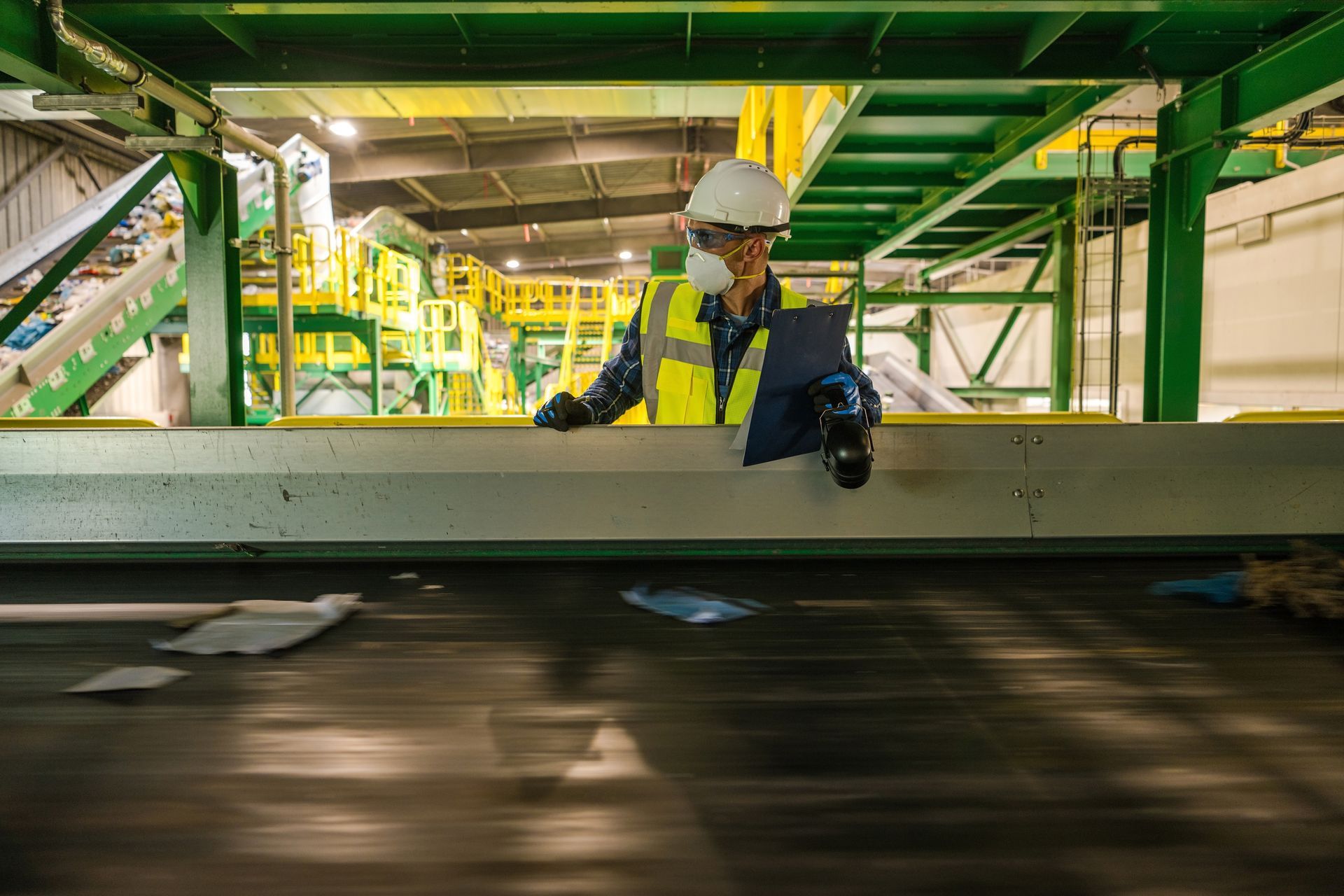 A Man Wearing a Hard Hat and Safety Vest is Standing on a Conveyor Belt in a Factory.