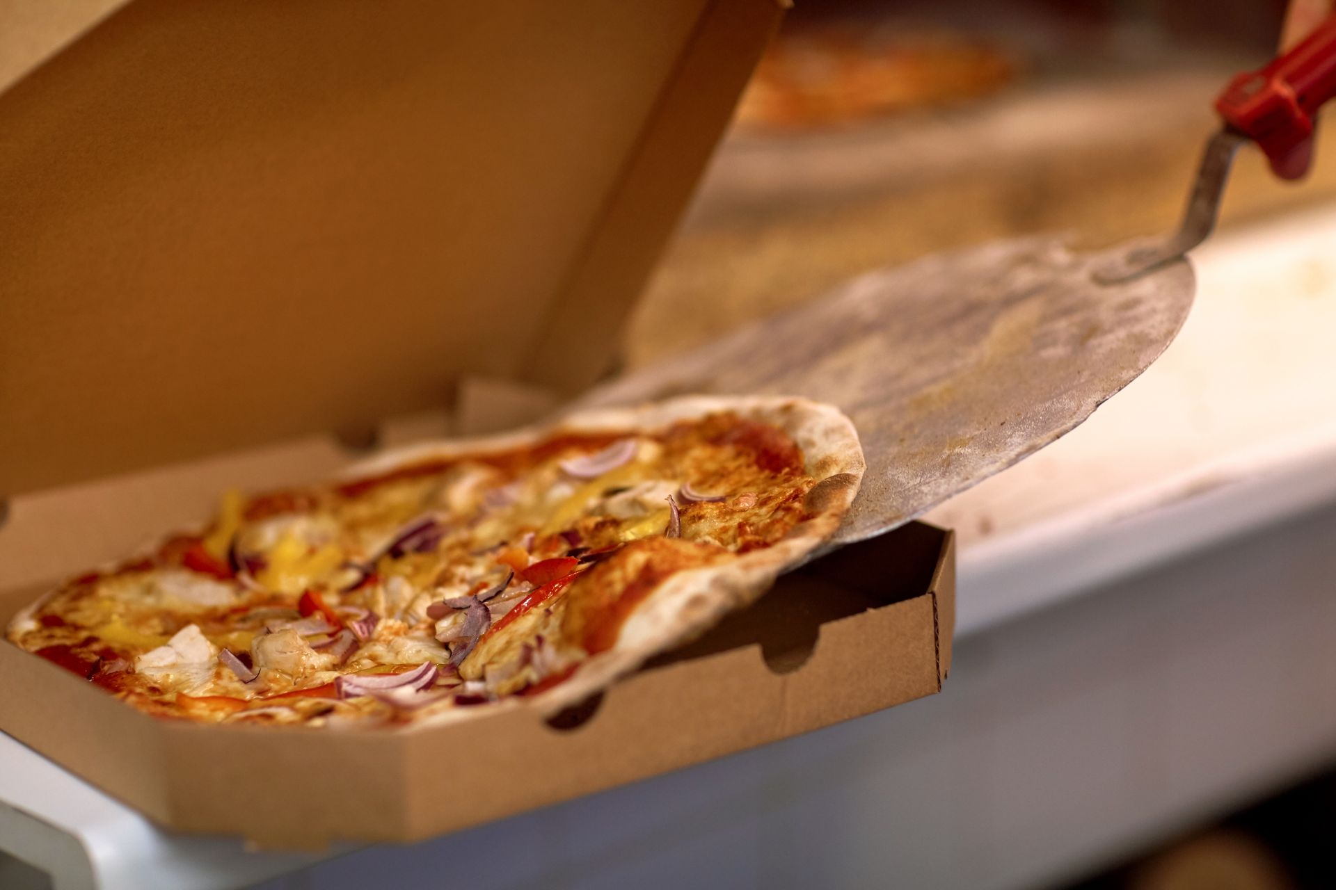 Pizza Being Placed in a Cardboard Box With a Pizza Peel — Romanas Italian Restaurant in Mermaid Beach, QLD