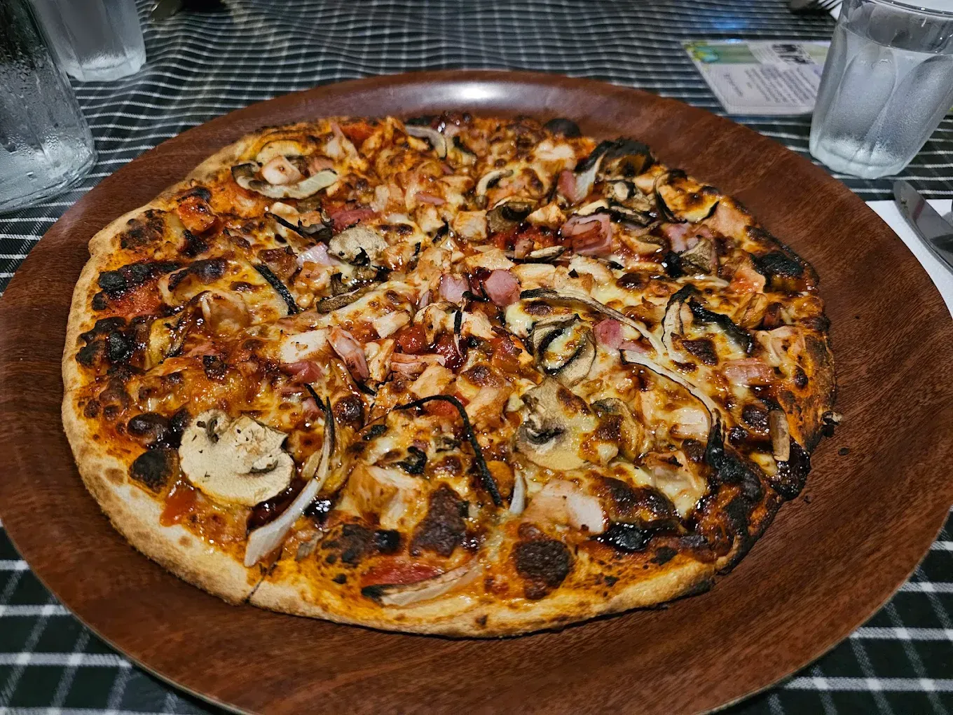 Pizza With Mushrooms, Onions, and Meat on a Brown Wooden Plate — Romanas Italian Restaurant in Mermaid Beach, QLD
