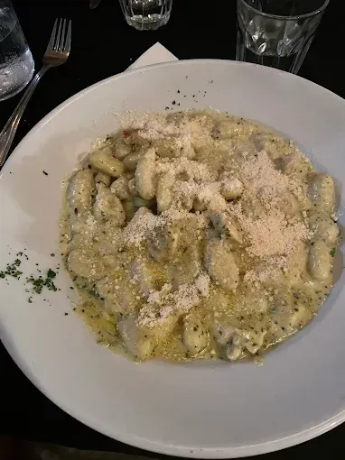 Plate of Creamy Gnocchi Pasta Topped With Grated Cheese on a Restaurant Table — Romanas Italian Restaurant in Mermaid Beach, QLD