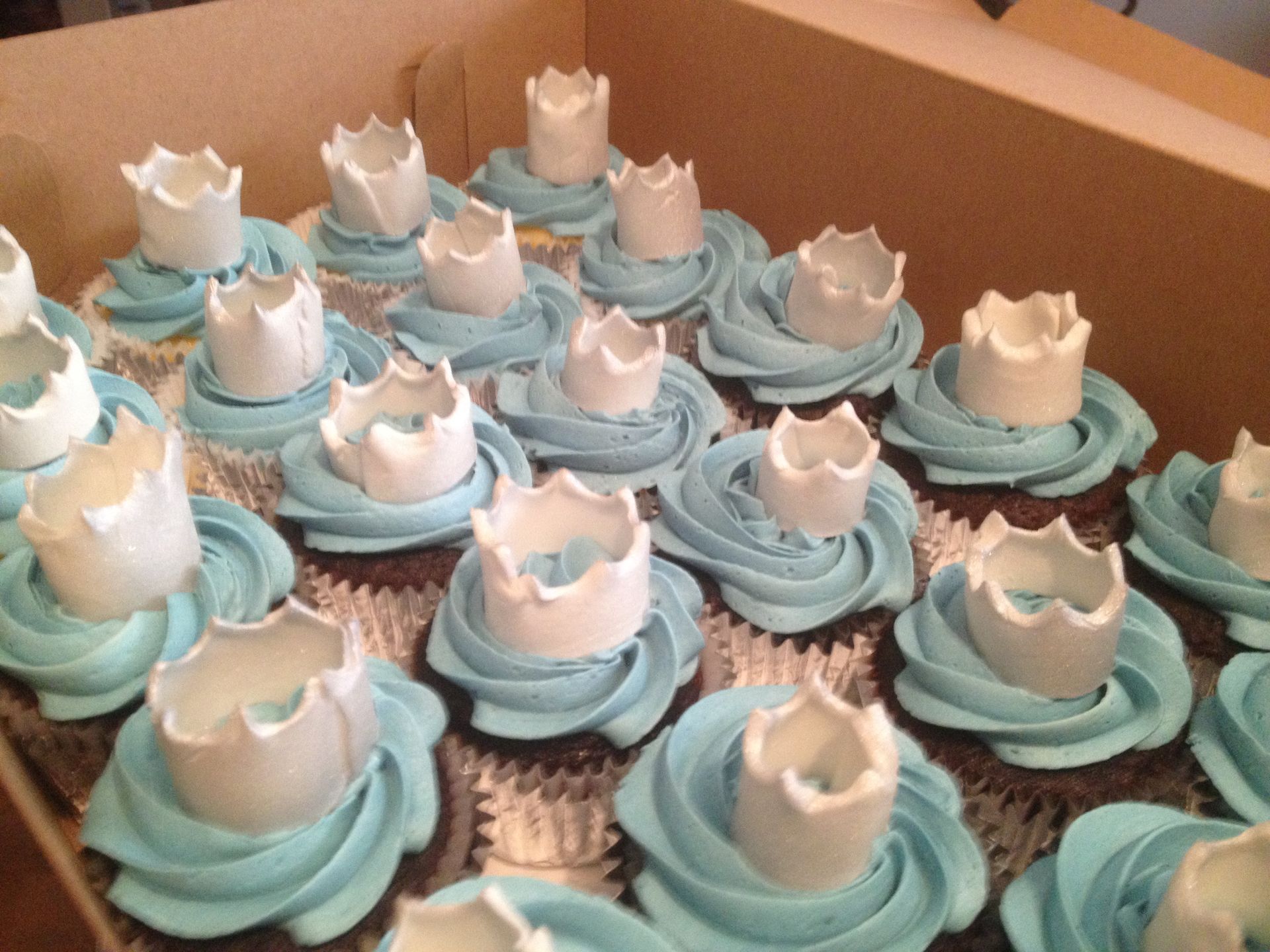 a box of cupcakes with blue frosting and white crowns on top