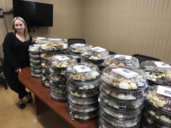 a woman is standing in front of a table filled with trays of cookies .