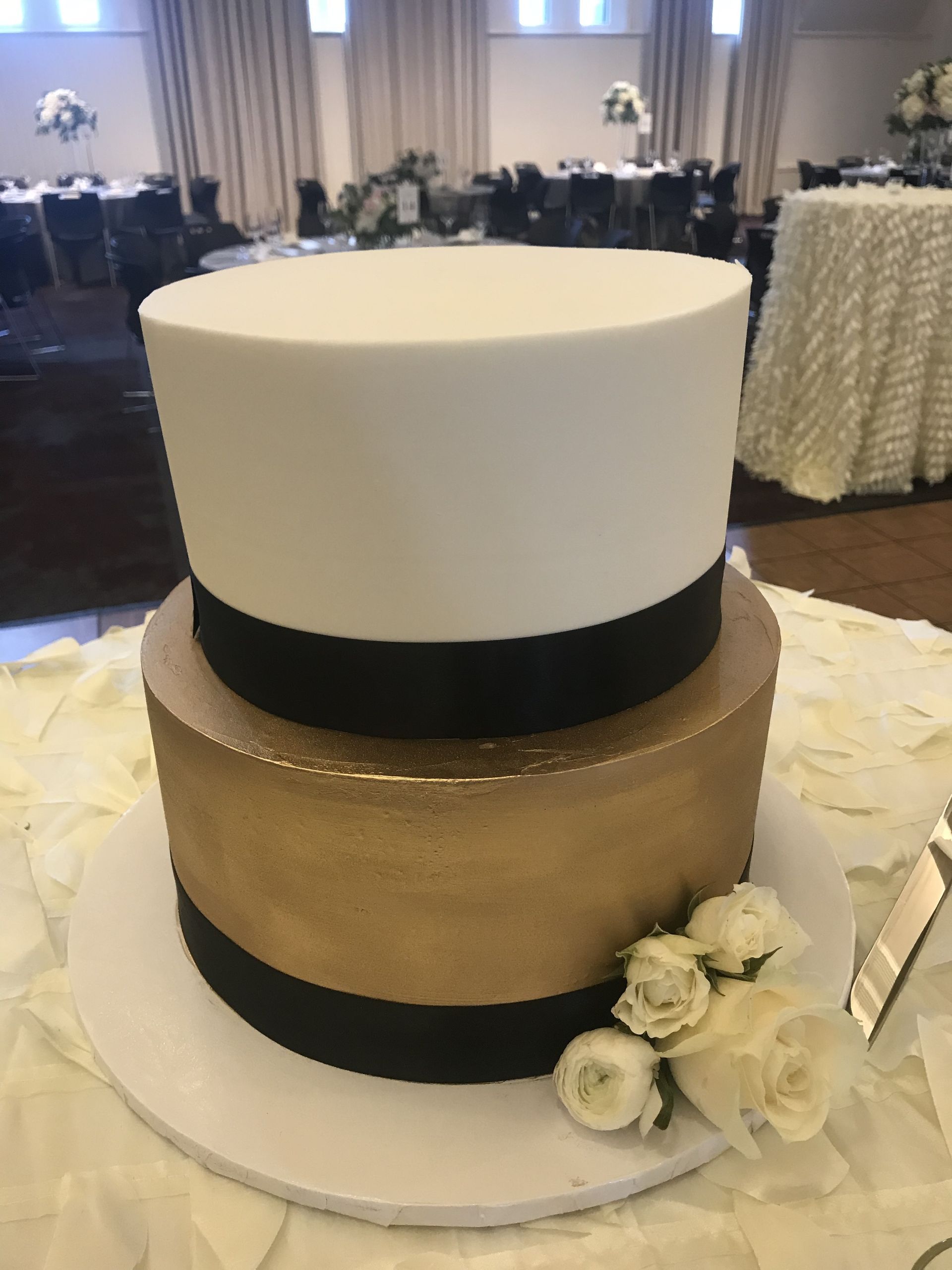 a black and gold wedding cake with white roses on top