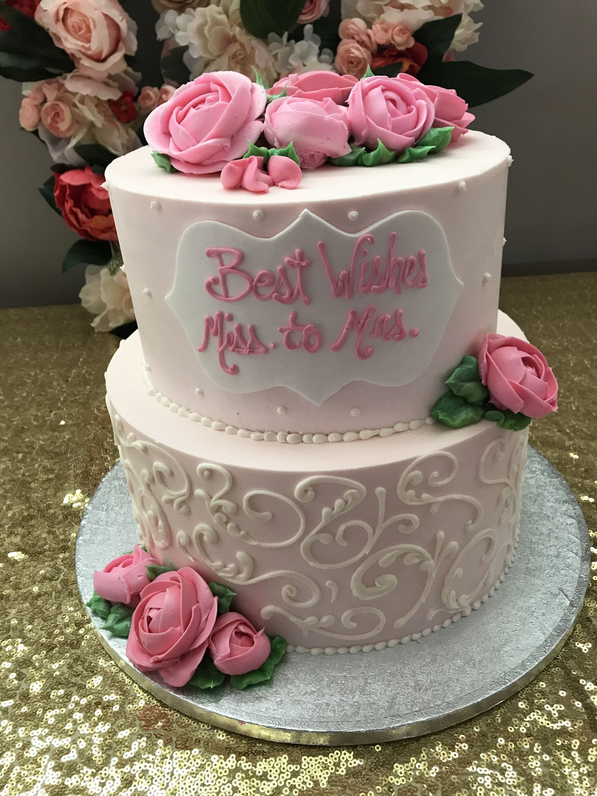 a two tiered cake with pink roses on top is on a table .