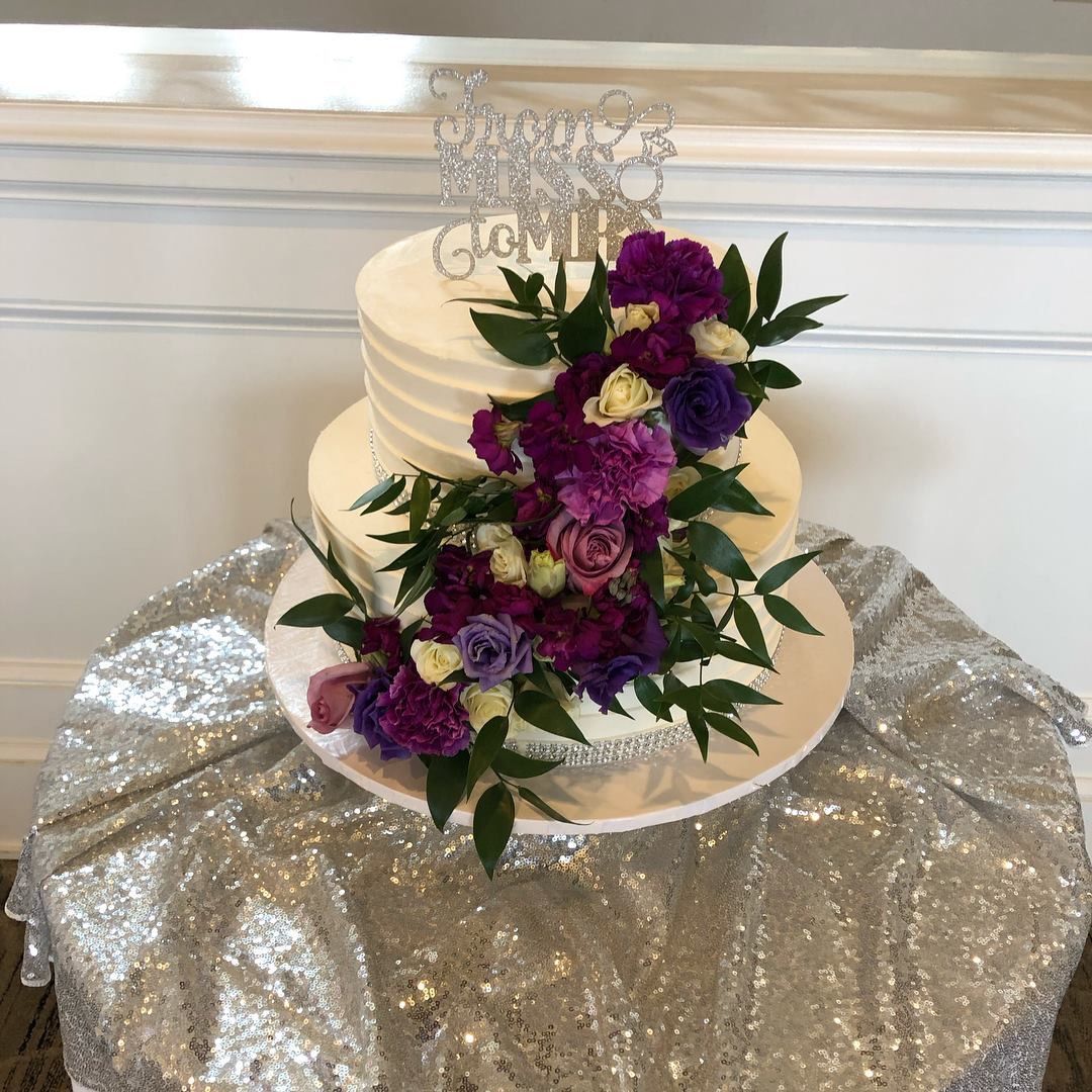 a wedding cake with purple flowers and a cake topper on a table .