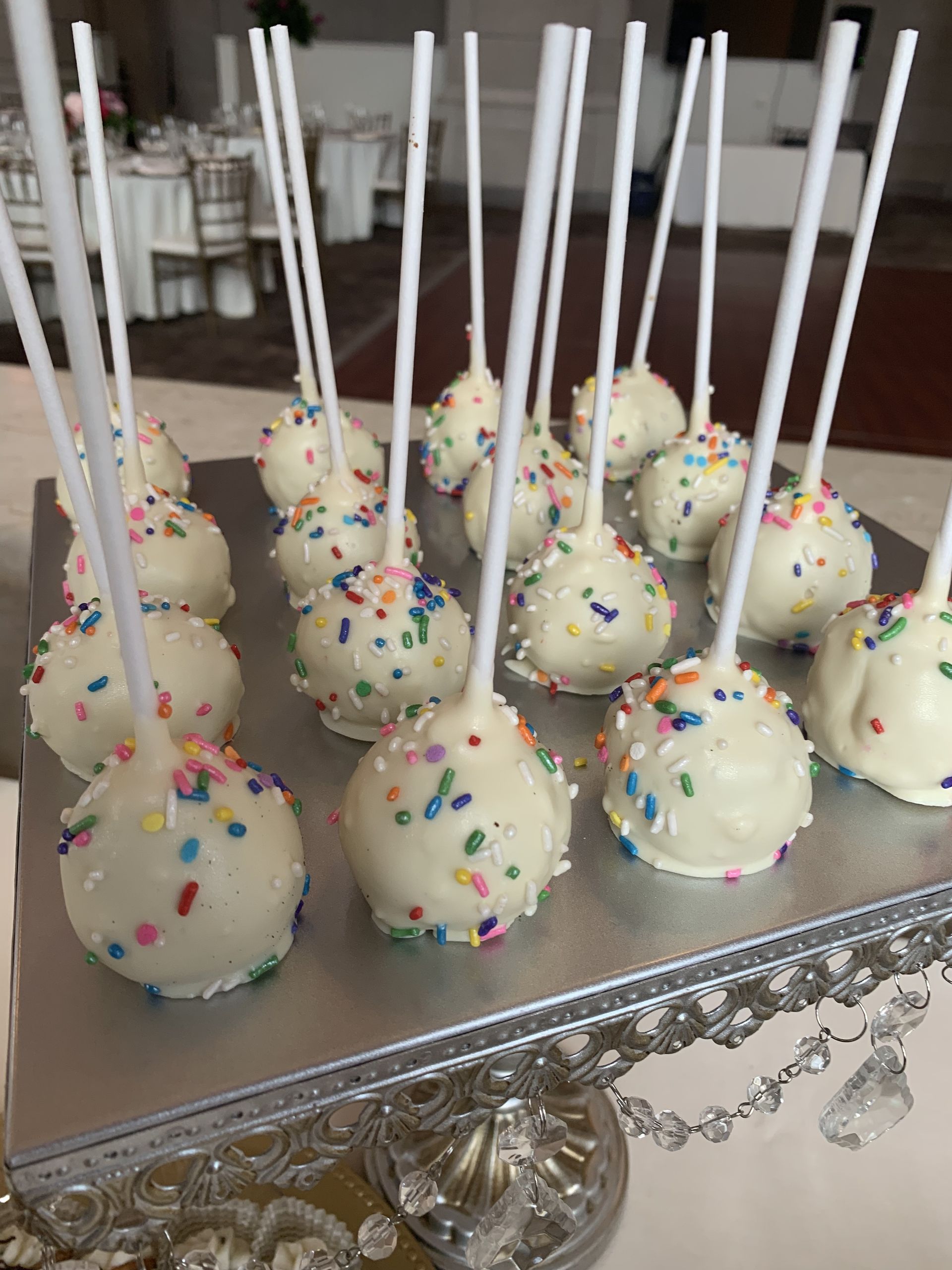 a bunch of cake pops with sprinkles on them on a silver plate .
