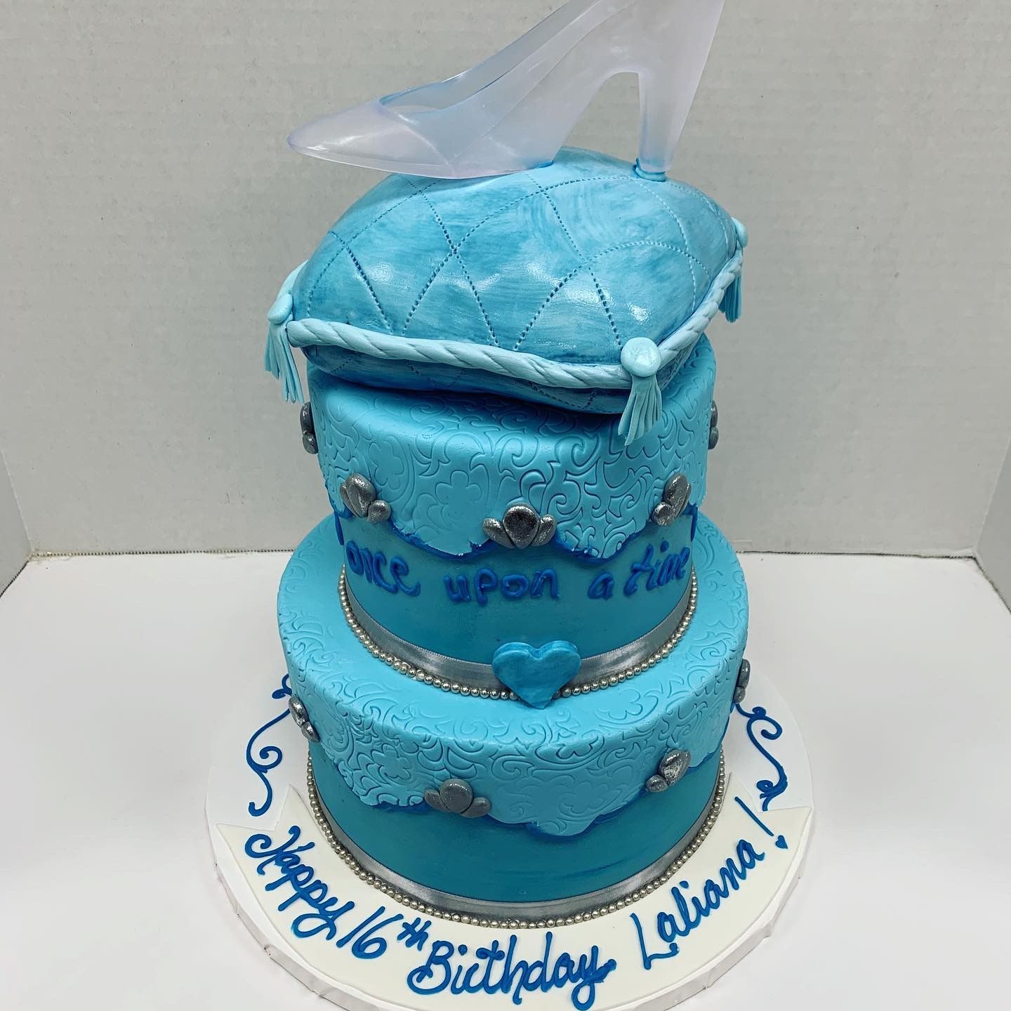 a blue birthday cake with a cinderella shoe on top