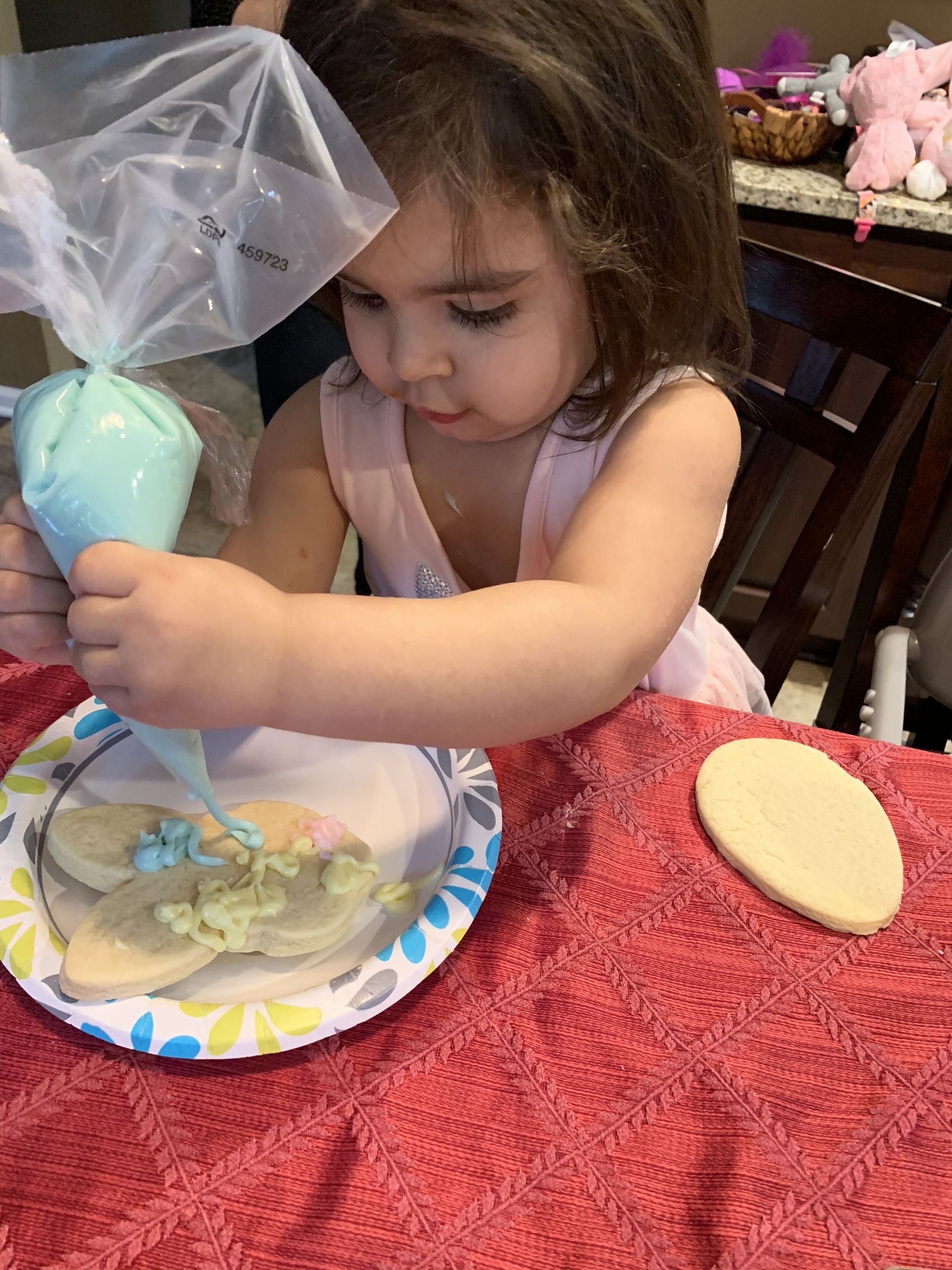 a little girl is icing a cookie on a paper plate .