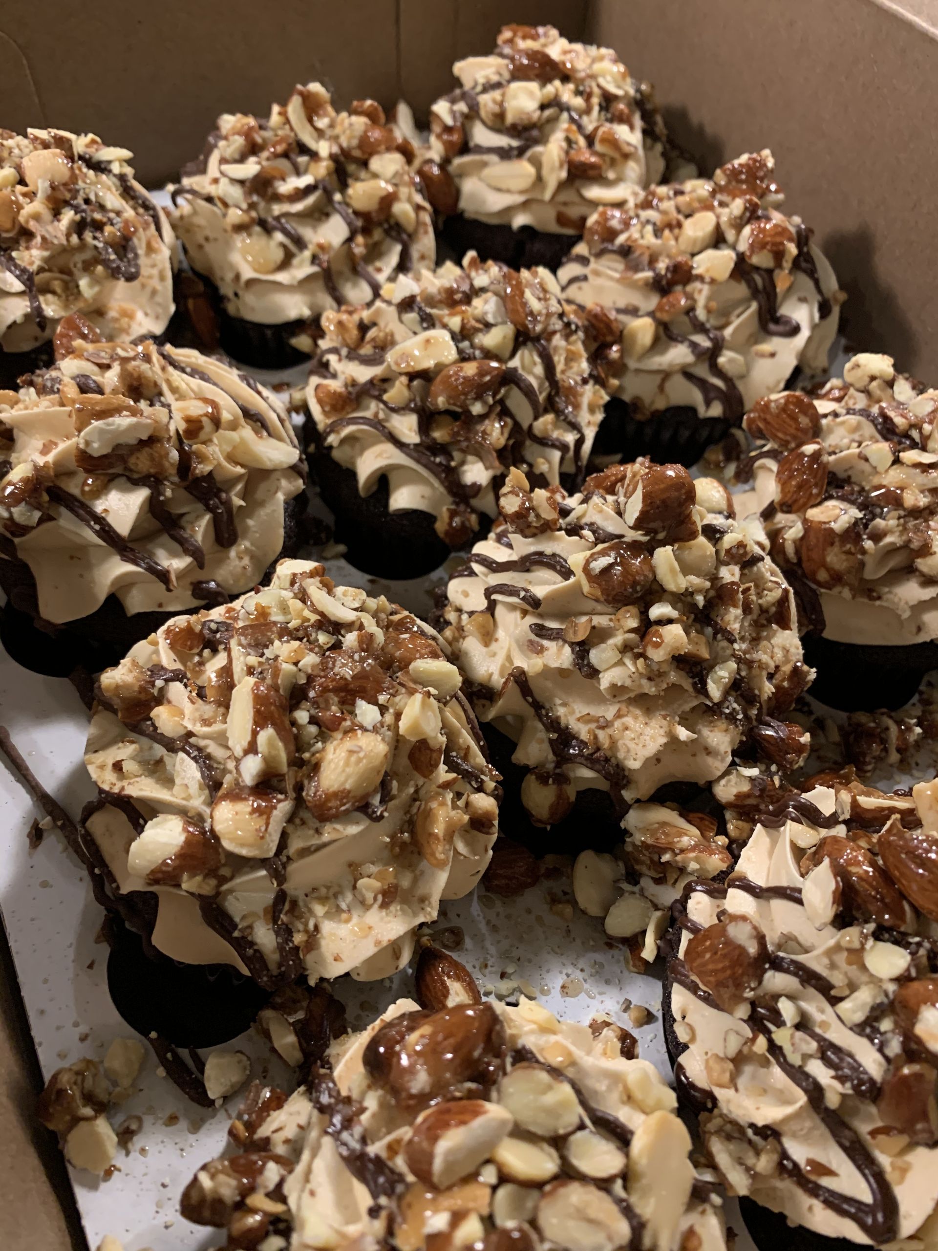 a box of cupcakes with chocolate frosting and nuts on top .