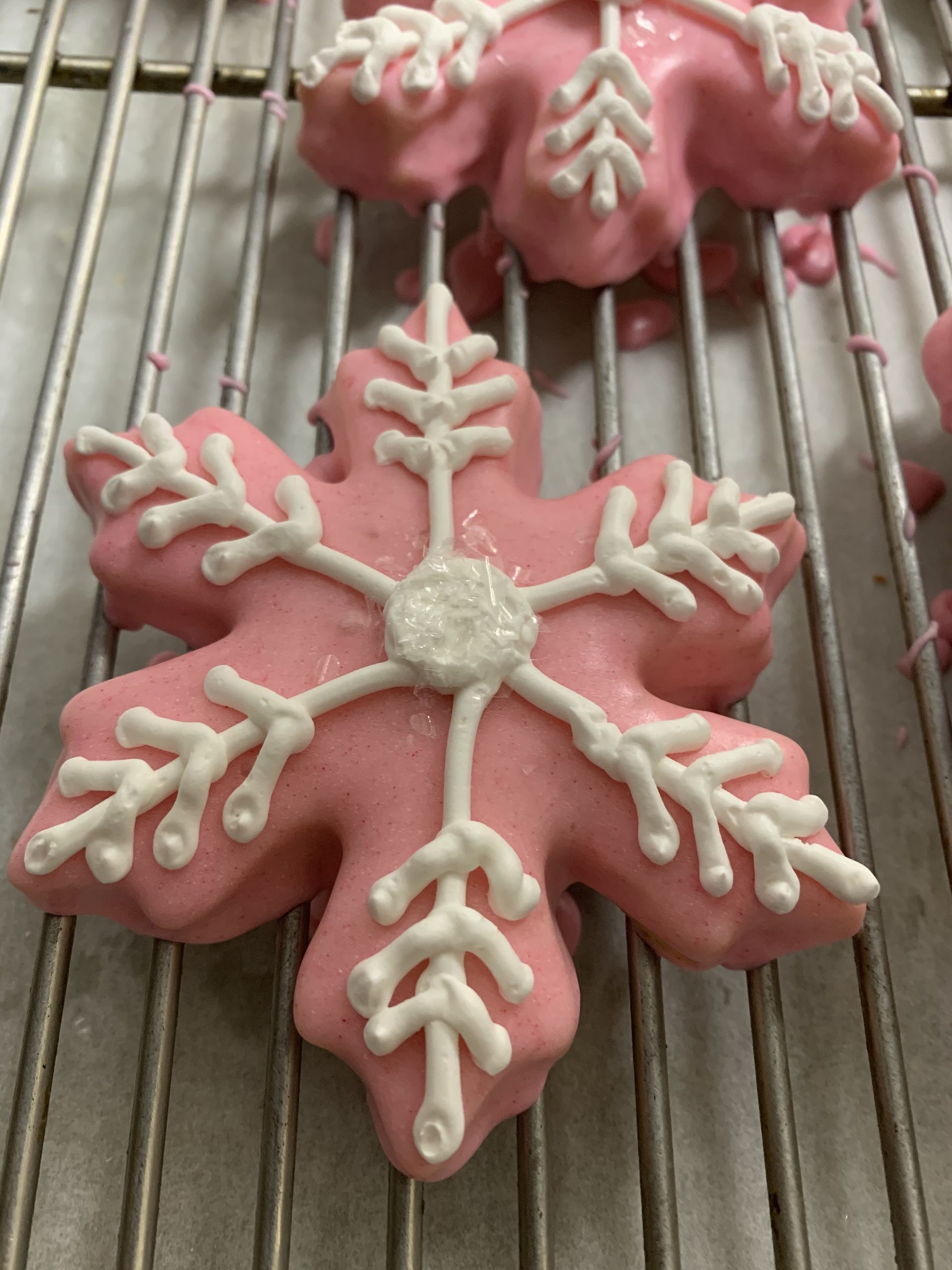 a pink snowflake cookie with white frosting is sitting on a cooling rack .