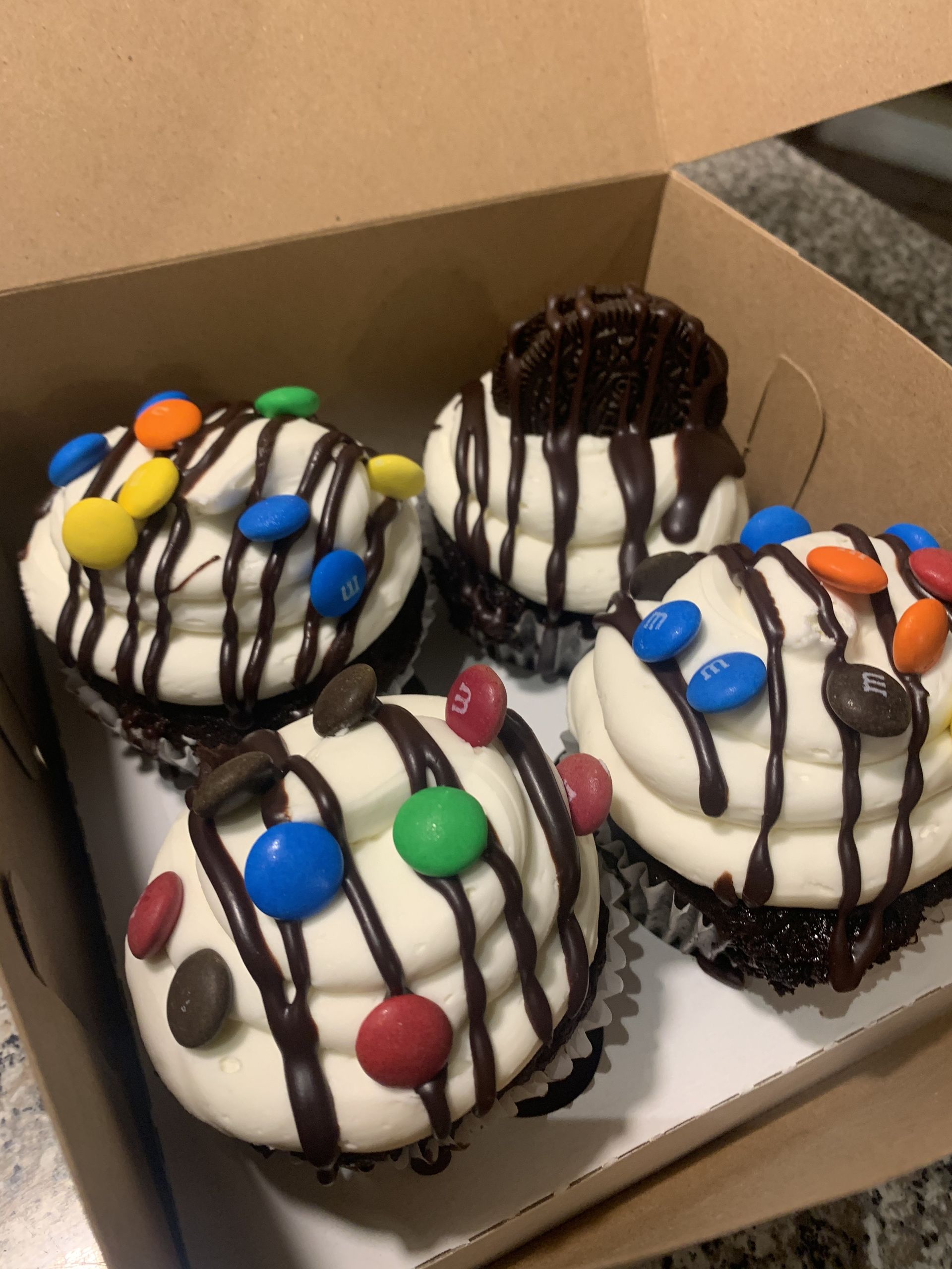 four cupcakes with chocolate frosting and m & m 's in a box