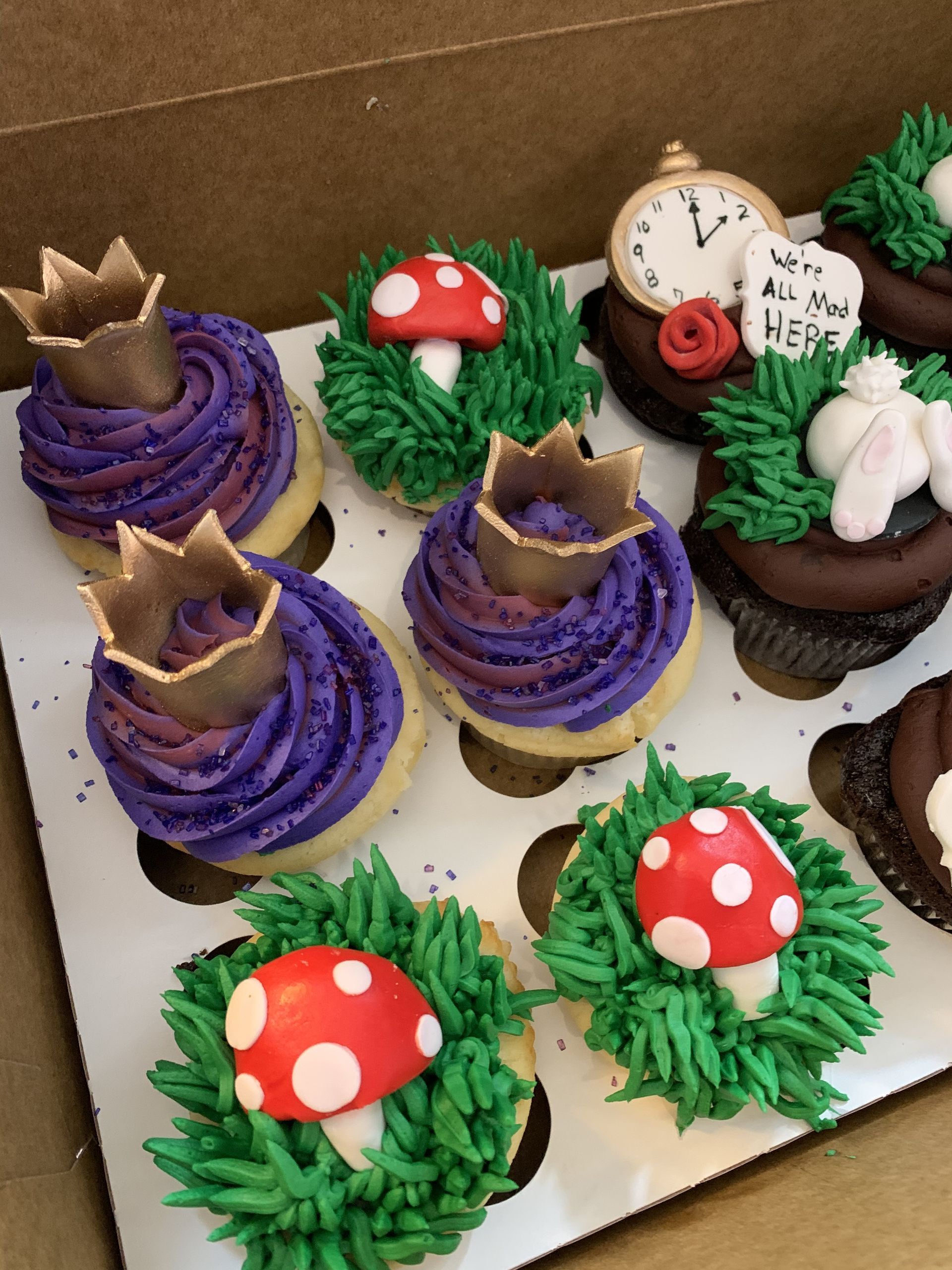 a box of alice in wonderland themed cupcakes