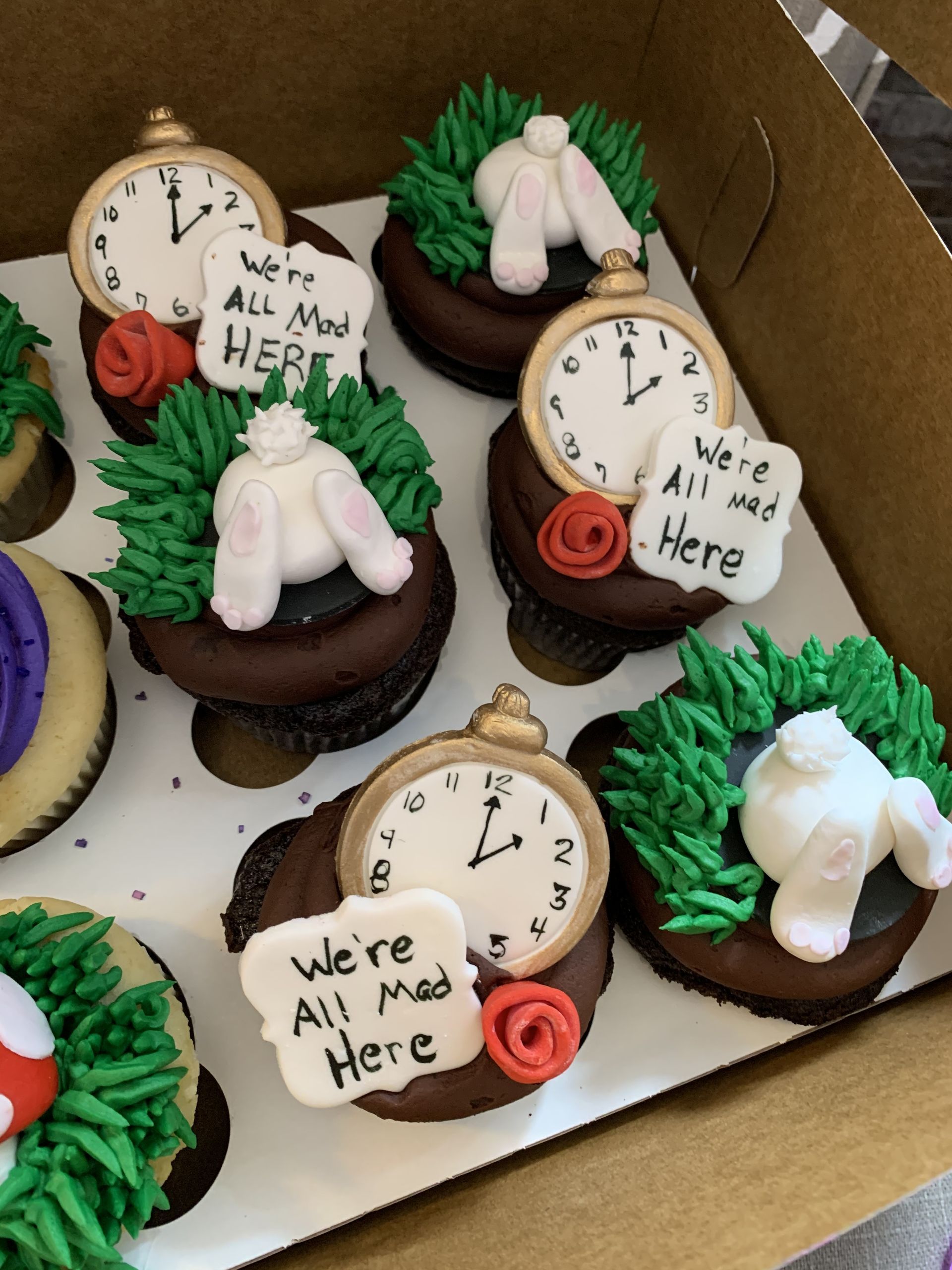 a box of alice in wonderland themed cupcakes