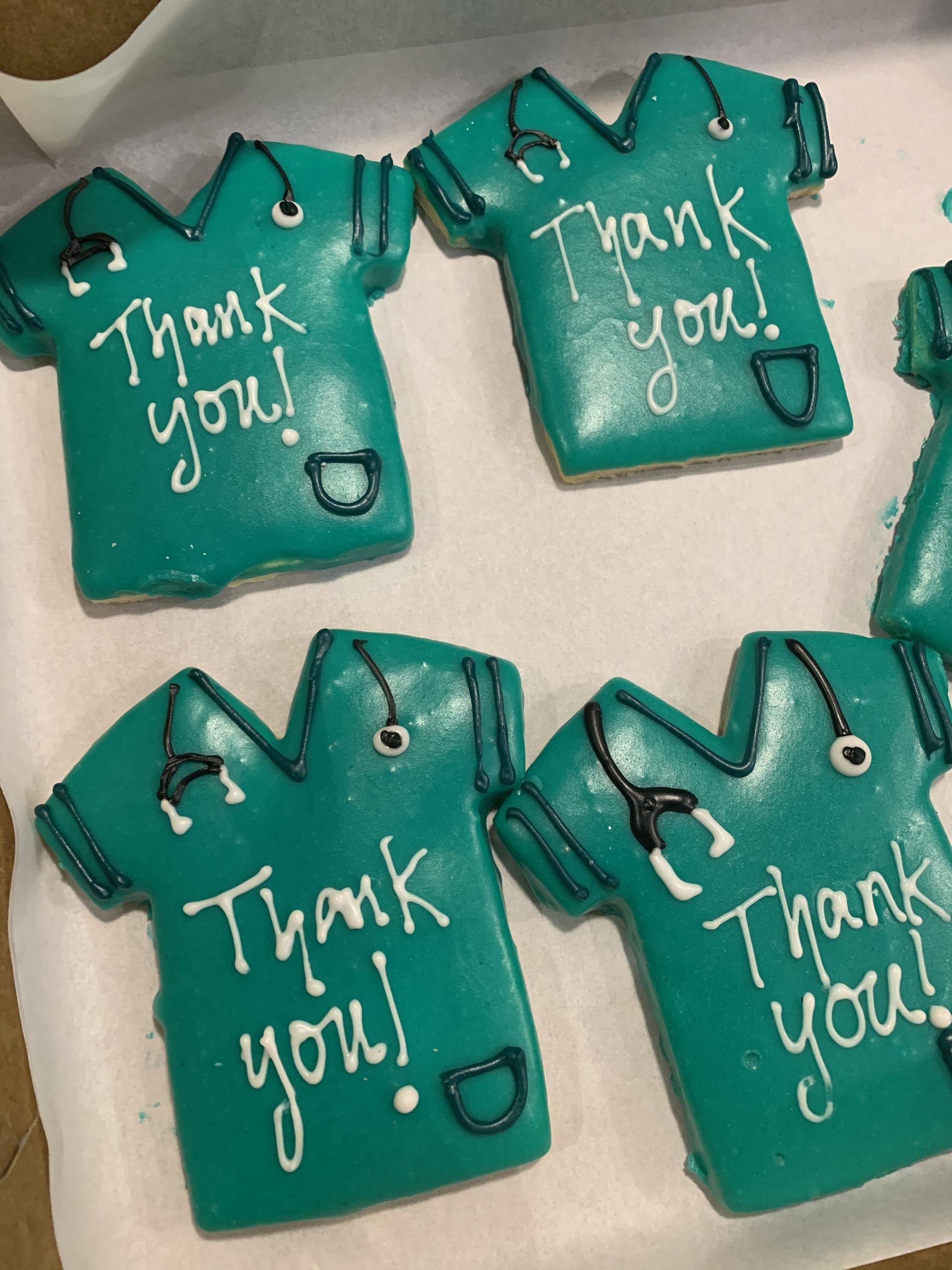 four cookies in the shape of scrub tops that say thank you