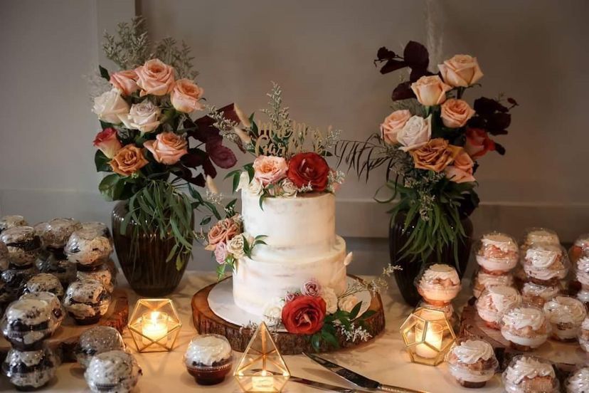 a wedding cake and cupcakes are on a table with flowers and candles .
