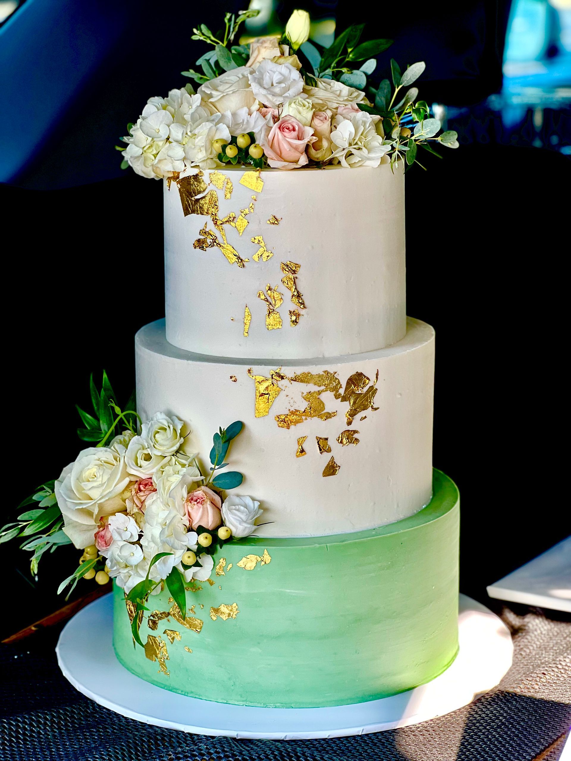 a three tiered wedding cake with flowers and gold leaf on it