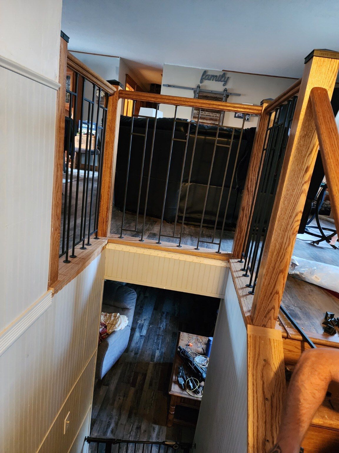 Stairwell with wooden railings and black metal balusters, view down to lower level opening.
