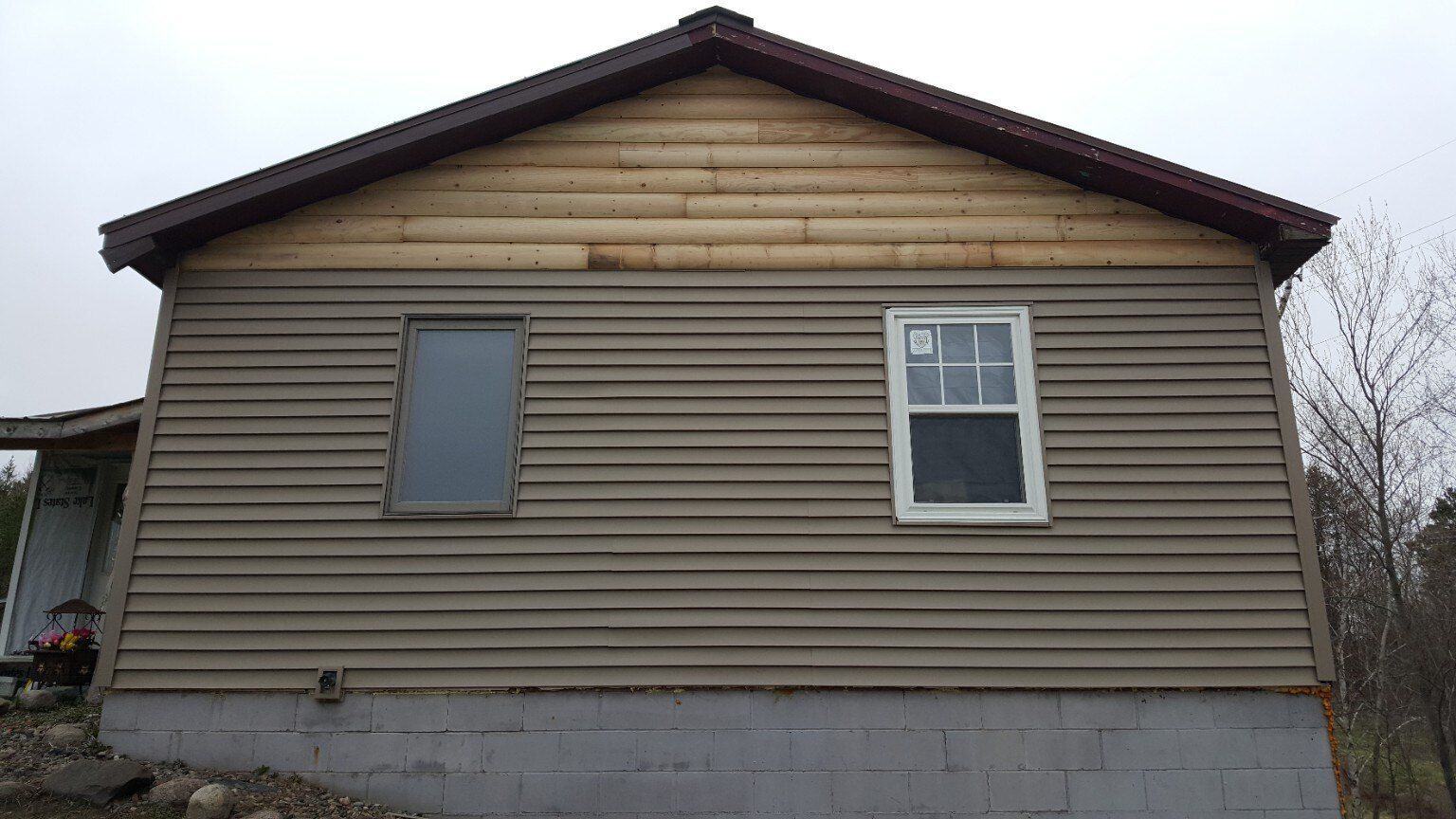 Side view of a beige house with brown trim, two windows, and a concrete foundation.