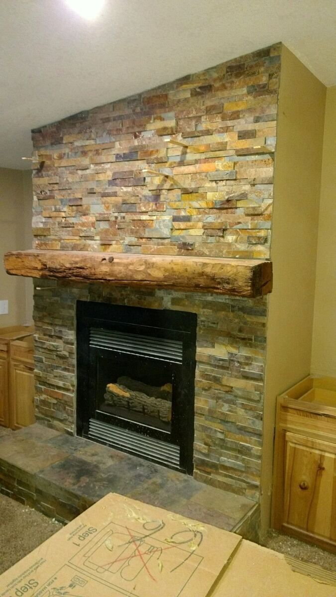Stone fireplace with black insert in a room with tan walls and wooden trim.