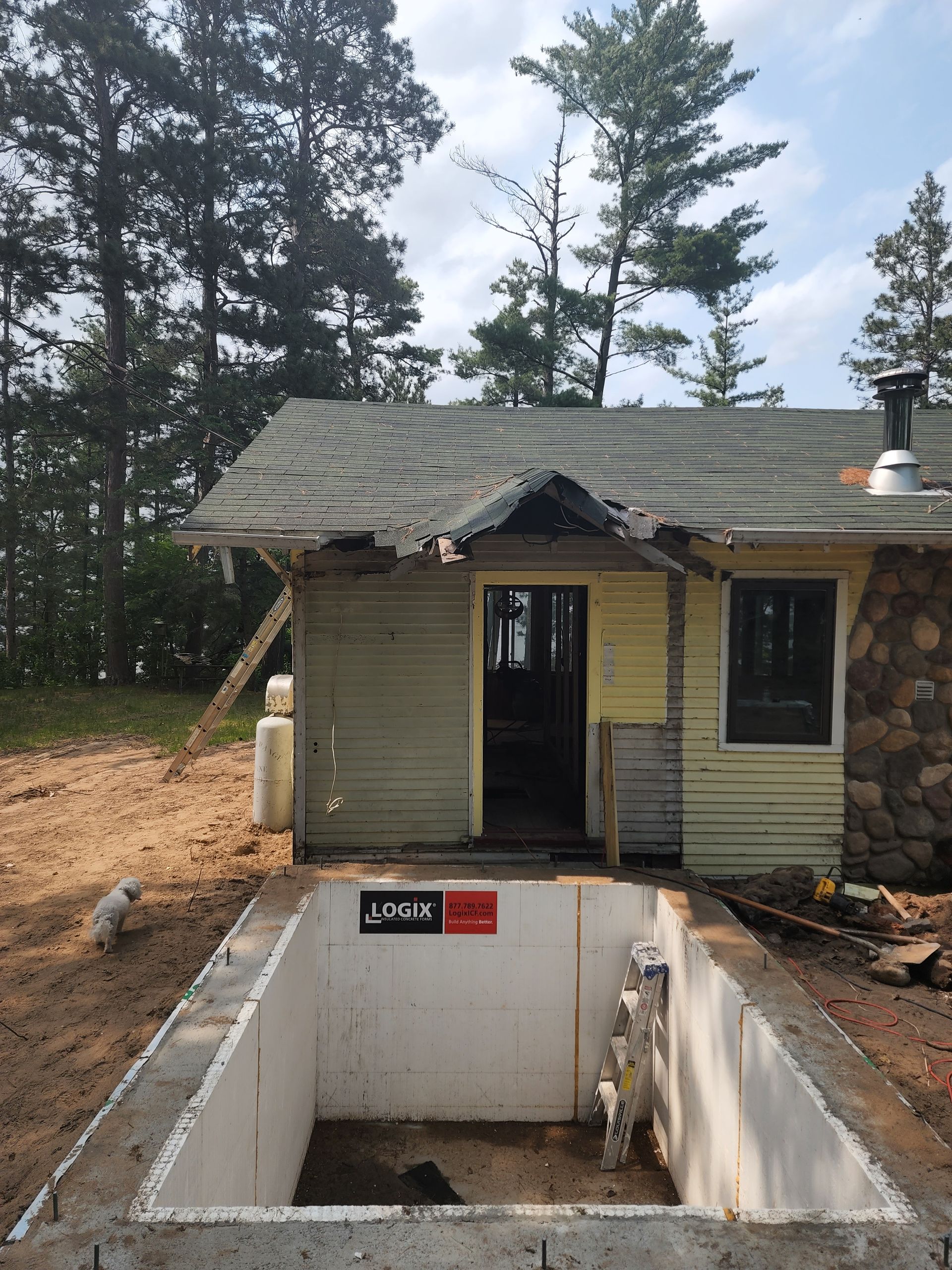 Small house with damaged roof and open basement in a wooded construction area
