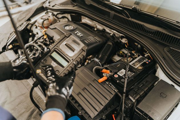 Mechanic working on a car engine with a diagnostic tool and battery in the engine bay
