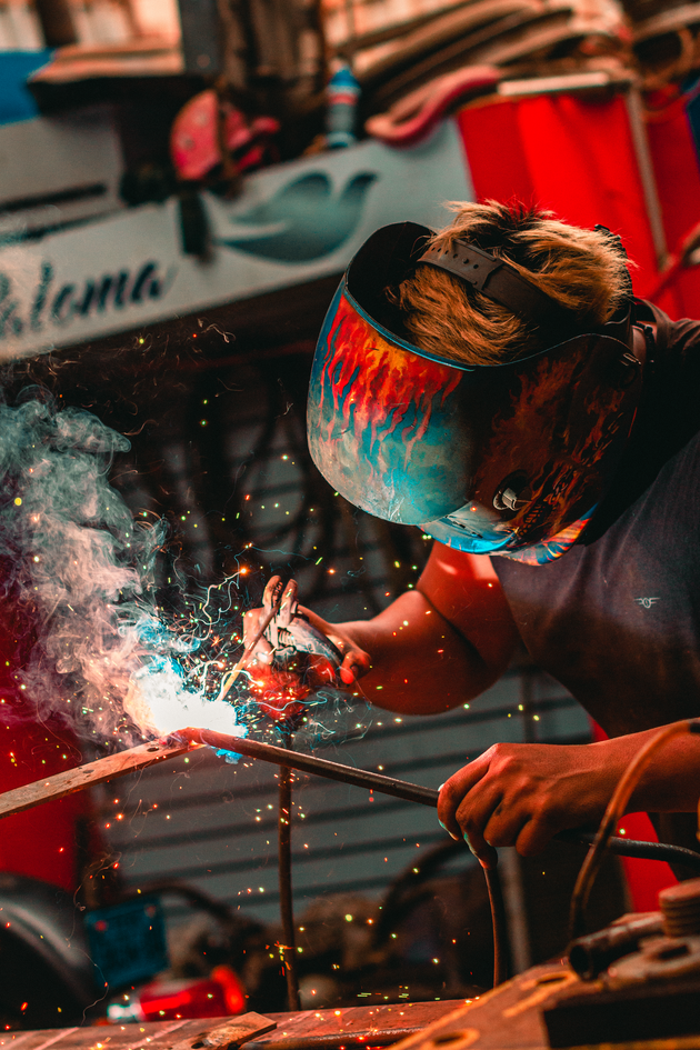 Welder in face shield working on metal, with bright sparks in a workshop