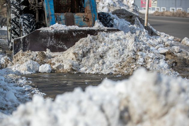 Snowplow pushing slushy snow along a road with piled snowbanks