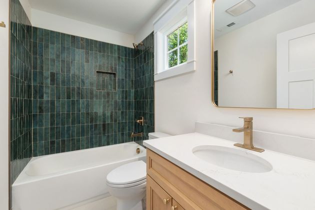 Modern bathroom with teal tile shower, white tub, and wood vanity with mirror