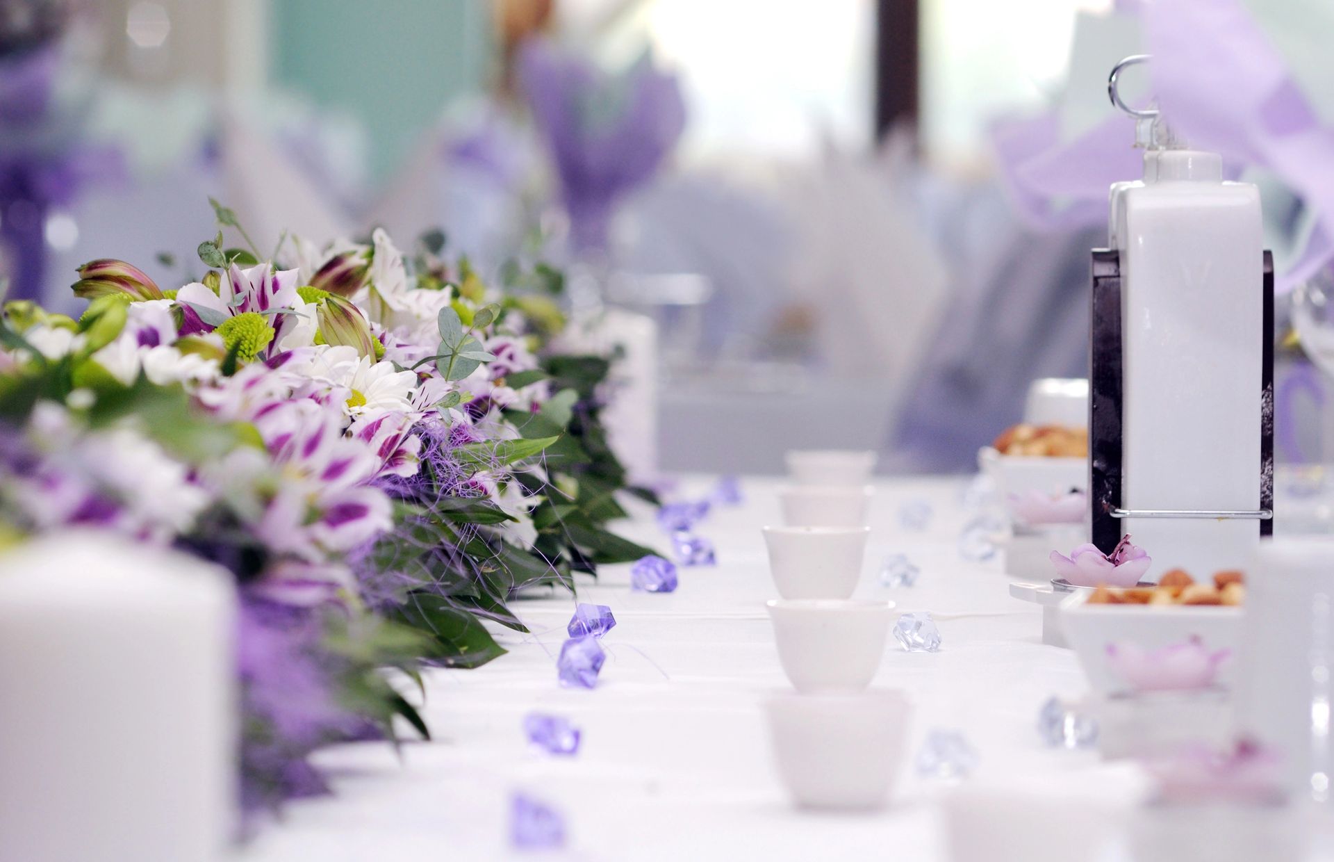 Una tavola apparecchiata con un centrotavola floreale viola e bianco, piccole ciotole bianche e pietre decorative viola sul tavolo.