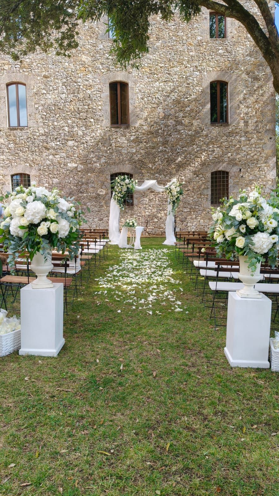 Un tavolo rotondo apparecchiato per un evento formale con tovaglie bianche, centrotavola floreali, candele e segnaposto.