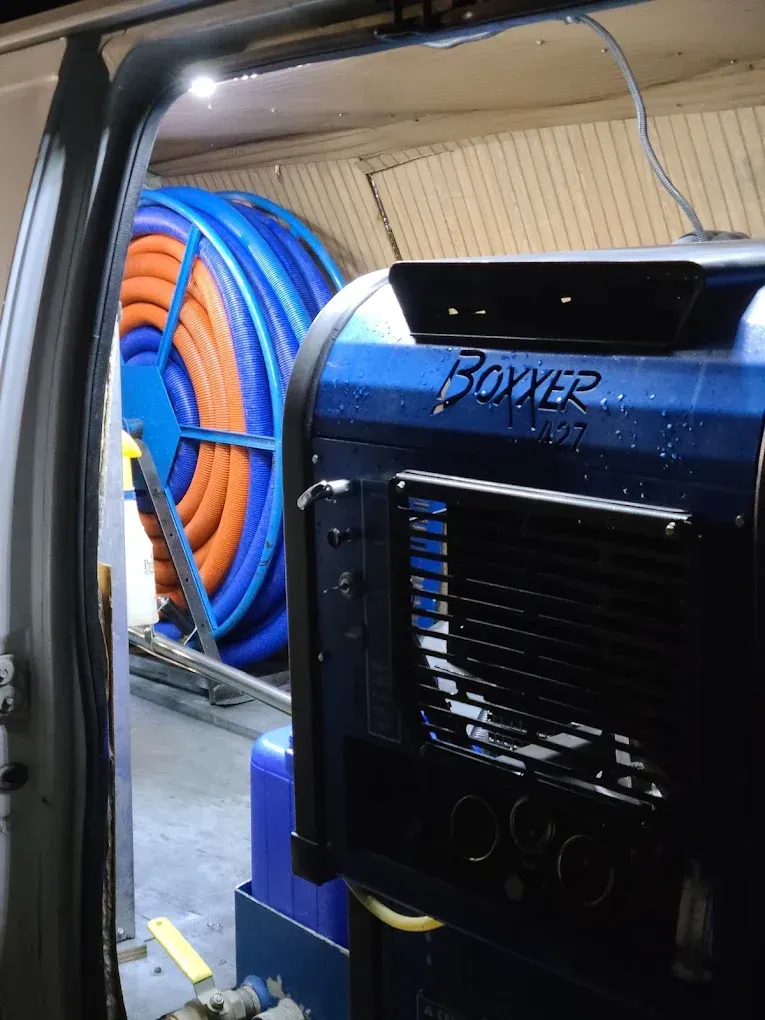 A blue Boxxer carpet cleaning machine and a large spool of orange and blue hose inside a work van.