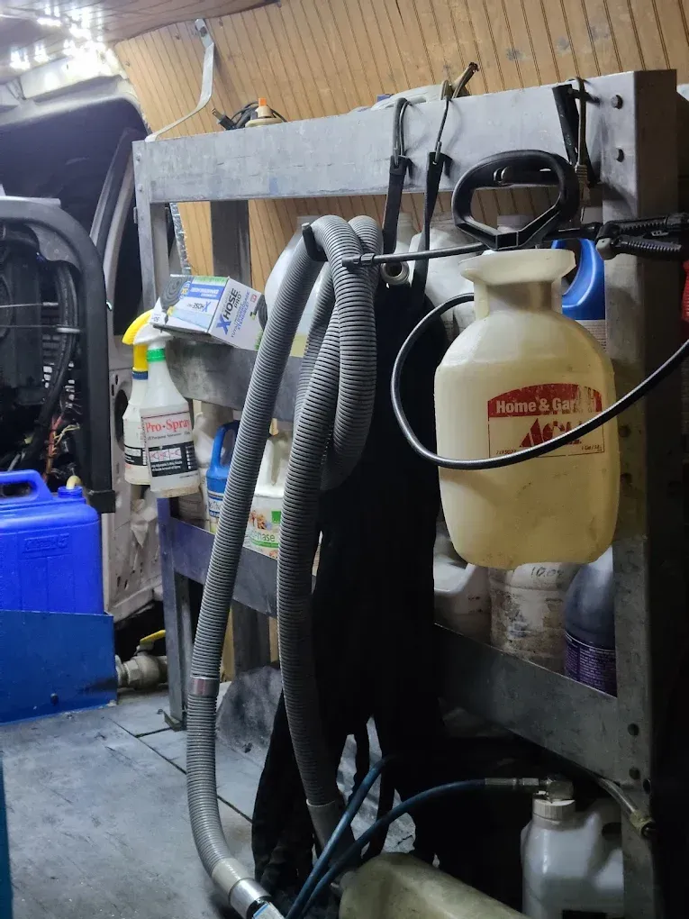 A utility shelf inside a vehicle, holding various spray bottles, cleaning equipment, hoses, and containers.