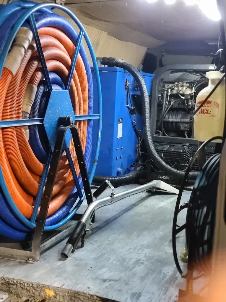 Interior of a work van equipped with a large blue hose reel, carpet cleaning wand, and industrial pump machinery.