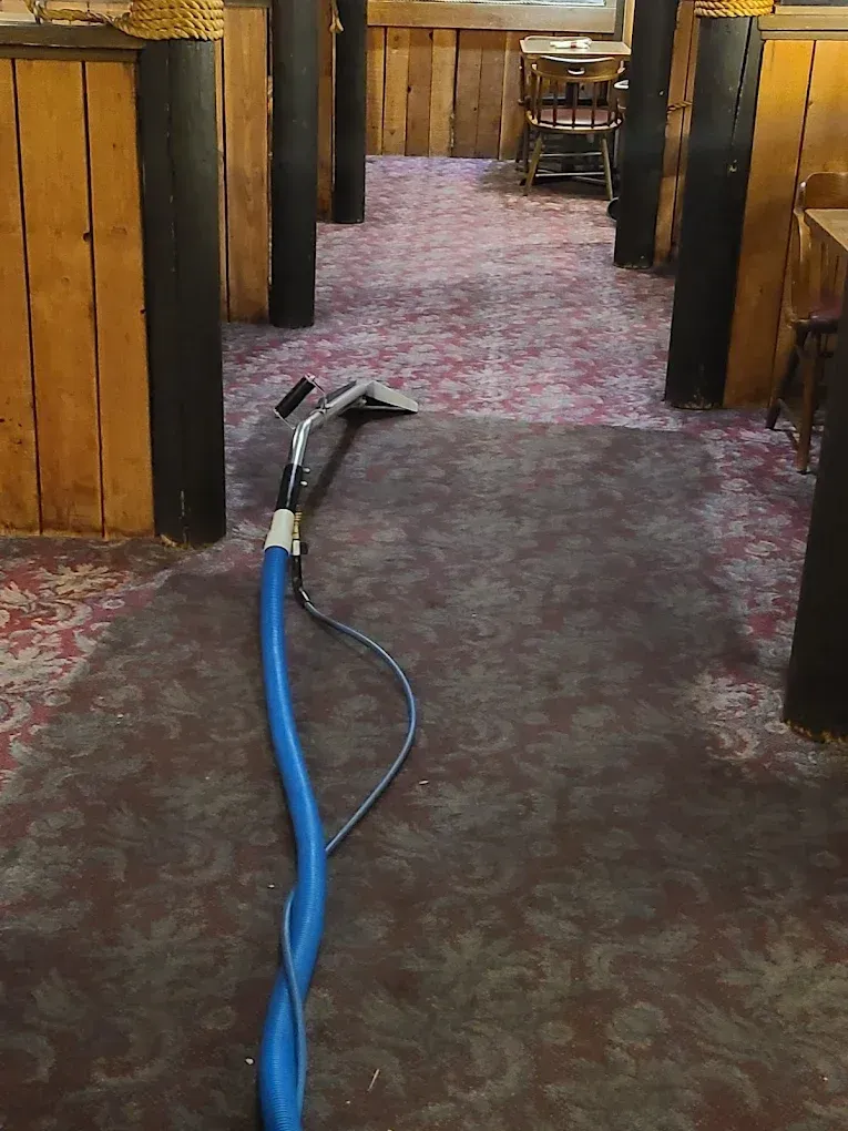 A carpet cleaning wand sits on a patterned carpet in a room with dark wood booths and pillars.