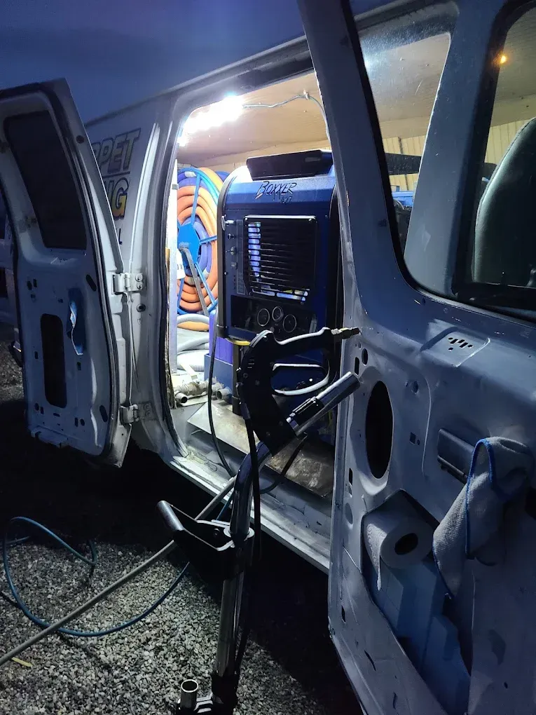 An open utility van at night containing a large blue industrial cleaning machine and coiled hoses.