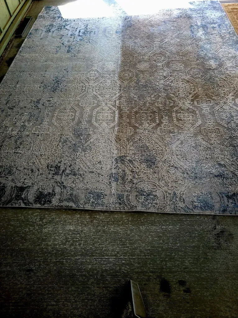 An area rug featuring an ornate, distressed-style damask pattern in shades of blue and tan, laid out on a concrete floor.