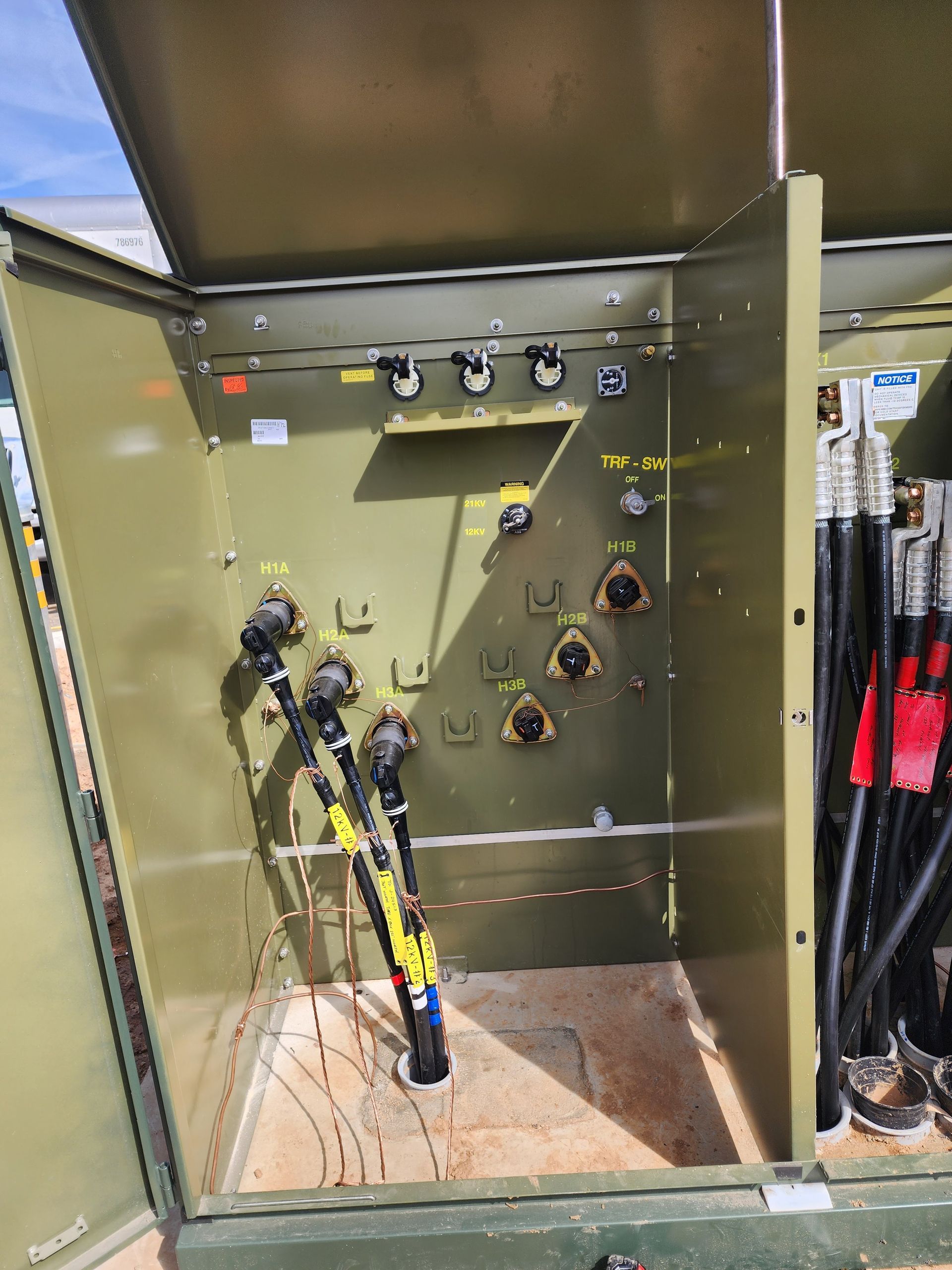 An open green utility pedestal showing electrical cable connections inside an outdoor equipment cabinet.