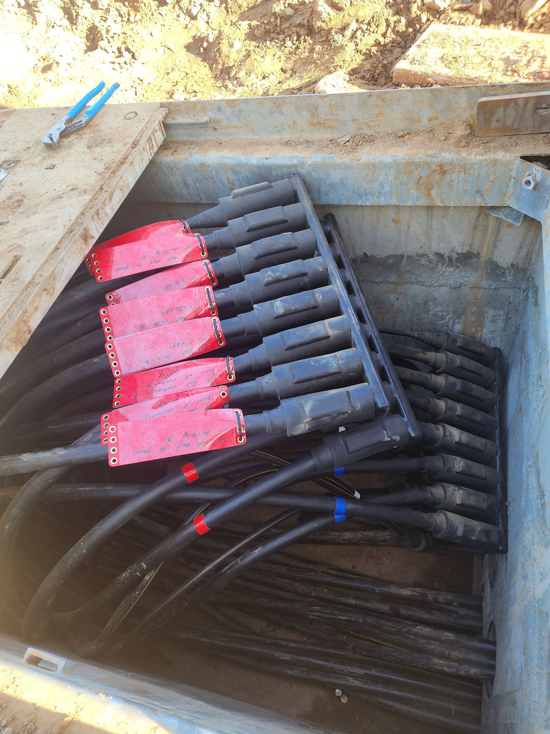 A view inside an electrical utility box showing heavy-duty black underground cables connected to a red-capped terminal bus.