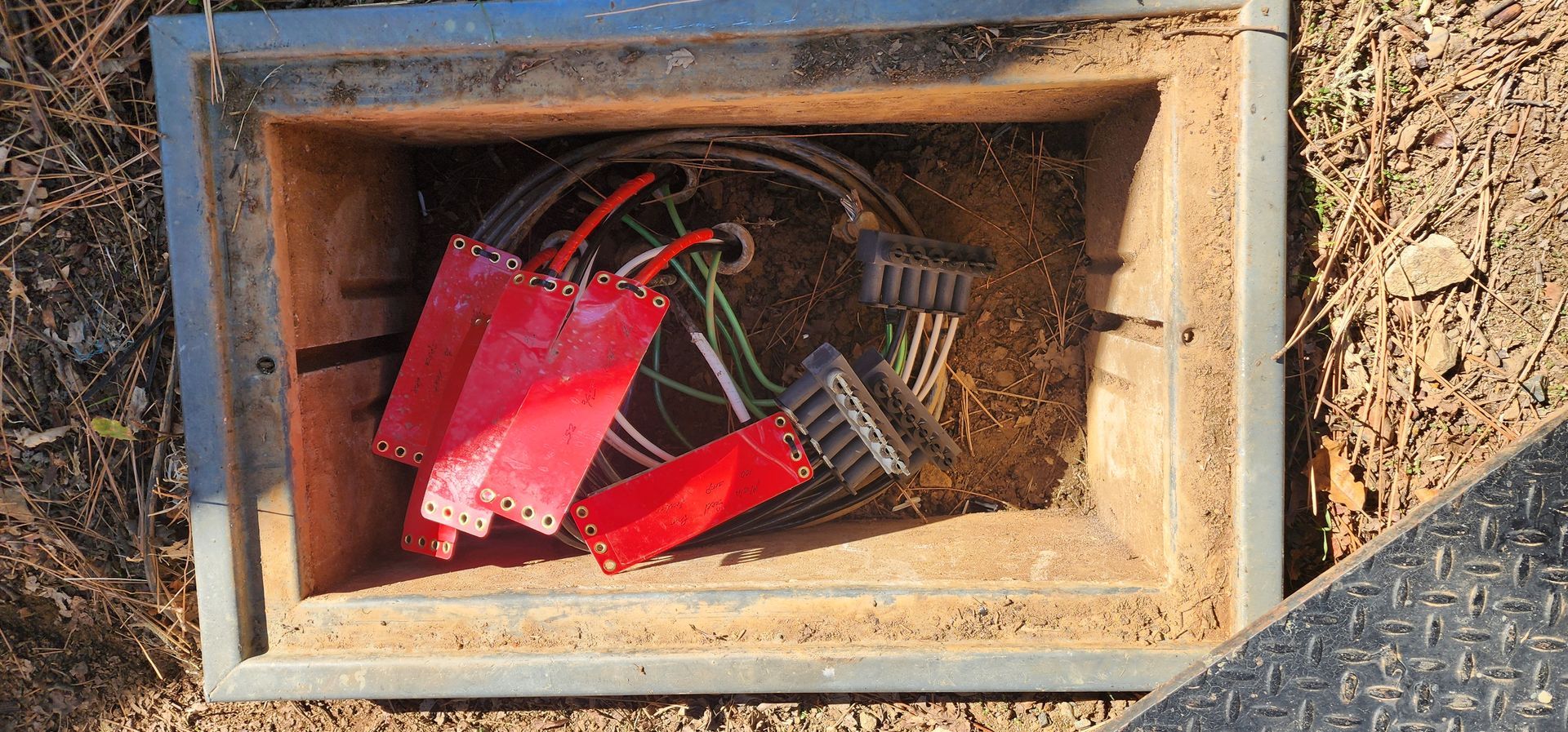 An open utility box in the ground containing several black electrical connectors with red plastic covers.