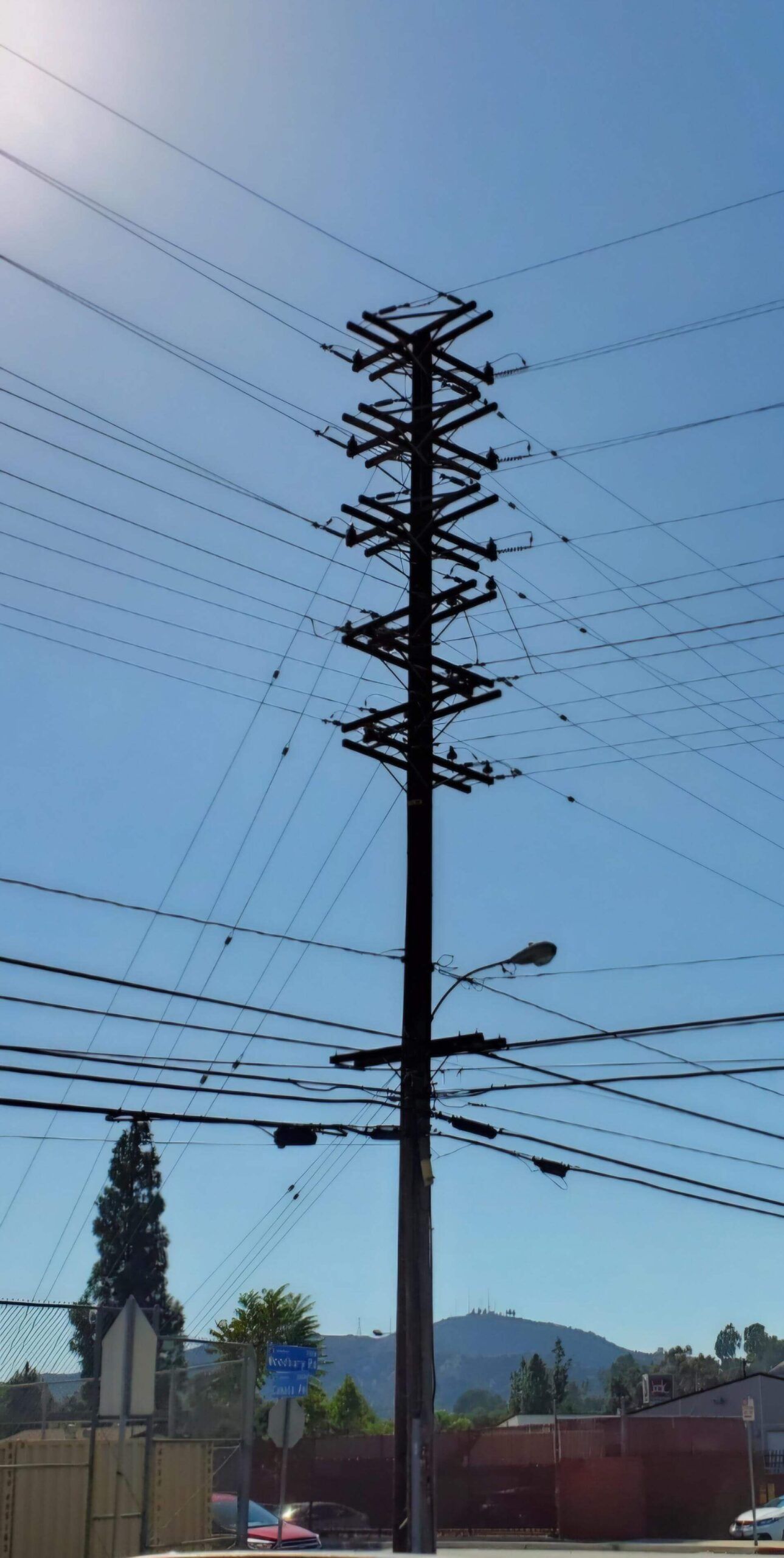 A tall utility pole stands against a clear blue sky, featuring multiple crossarms laden with numerous electrical wires.