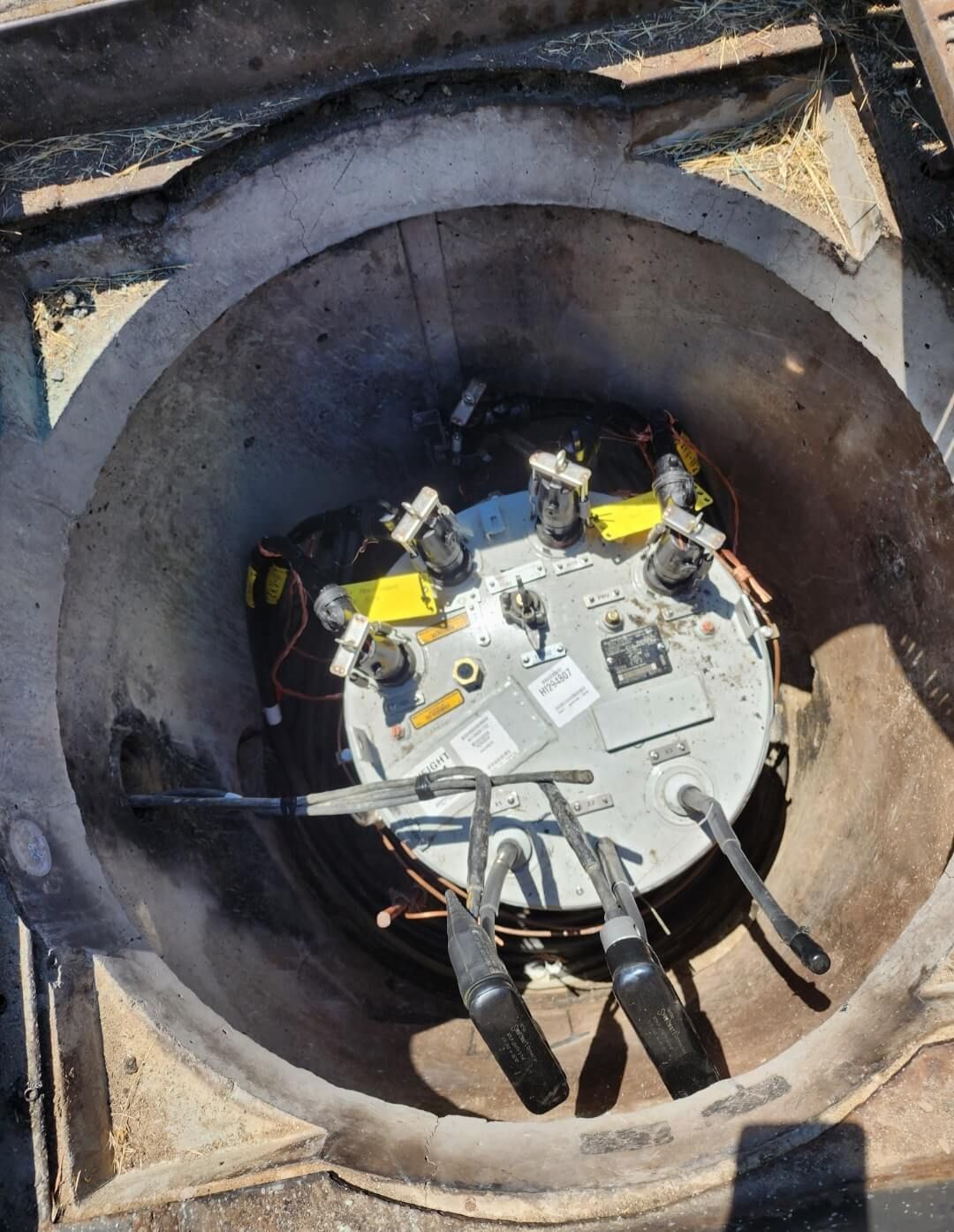 A round, electrical junction box housed inside a concrete underground enclosure with multiple cables connected to the top.