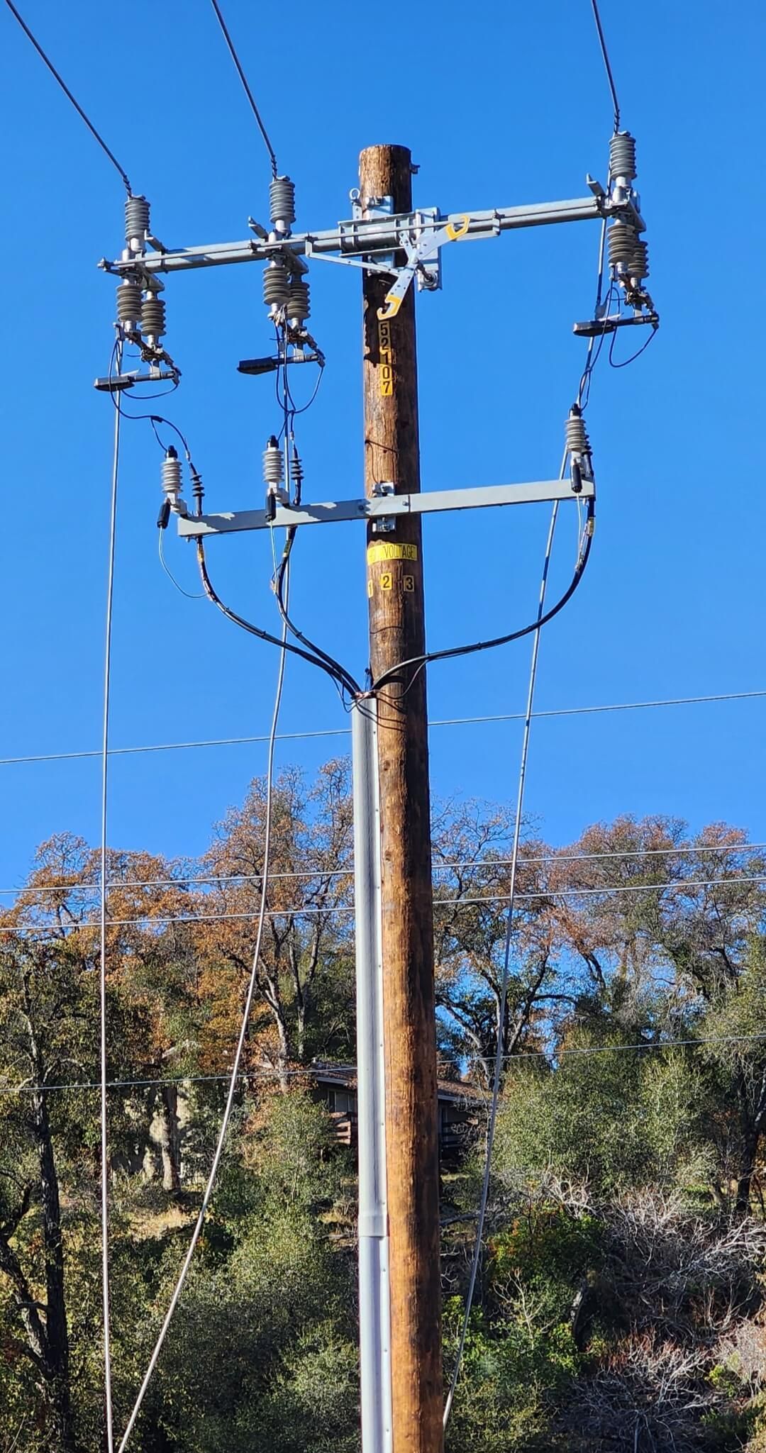 A wooden utility pole with three electrical insulators mounted on a crossarm against a clear blue sky.