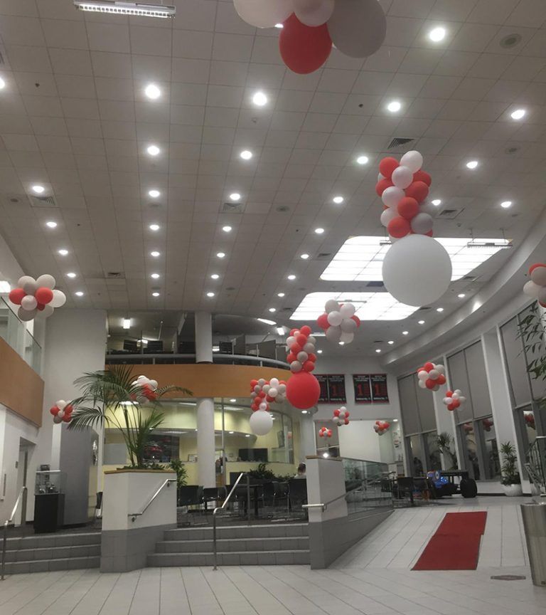Decorated indoor lobby with red and white balloons and a red carpet leading to a stage area